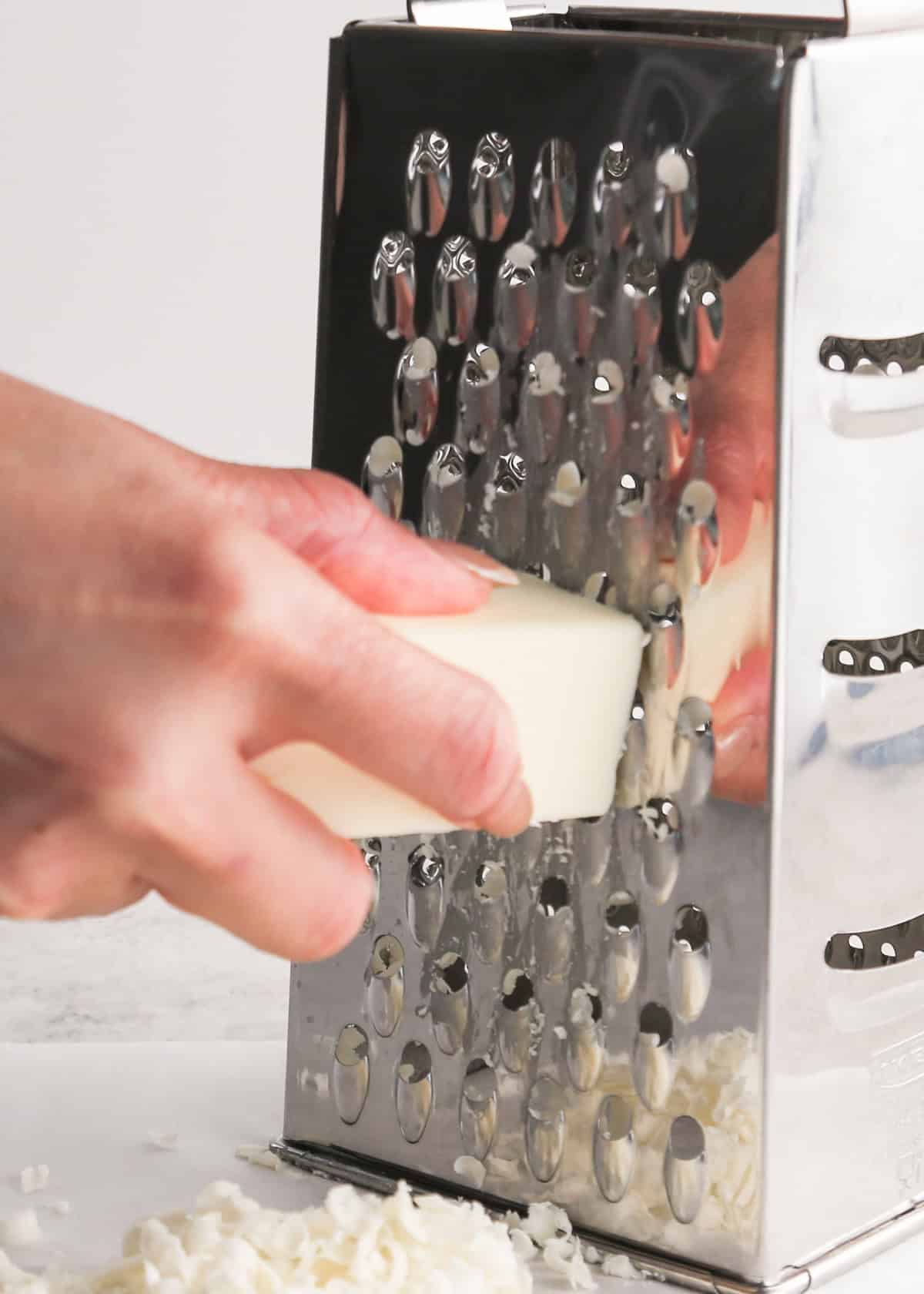 a hand grating frozen butter on a silver box grater