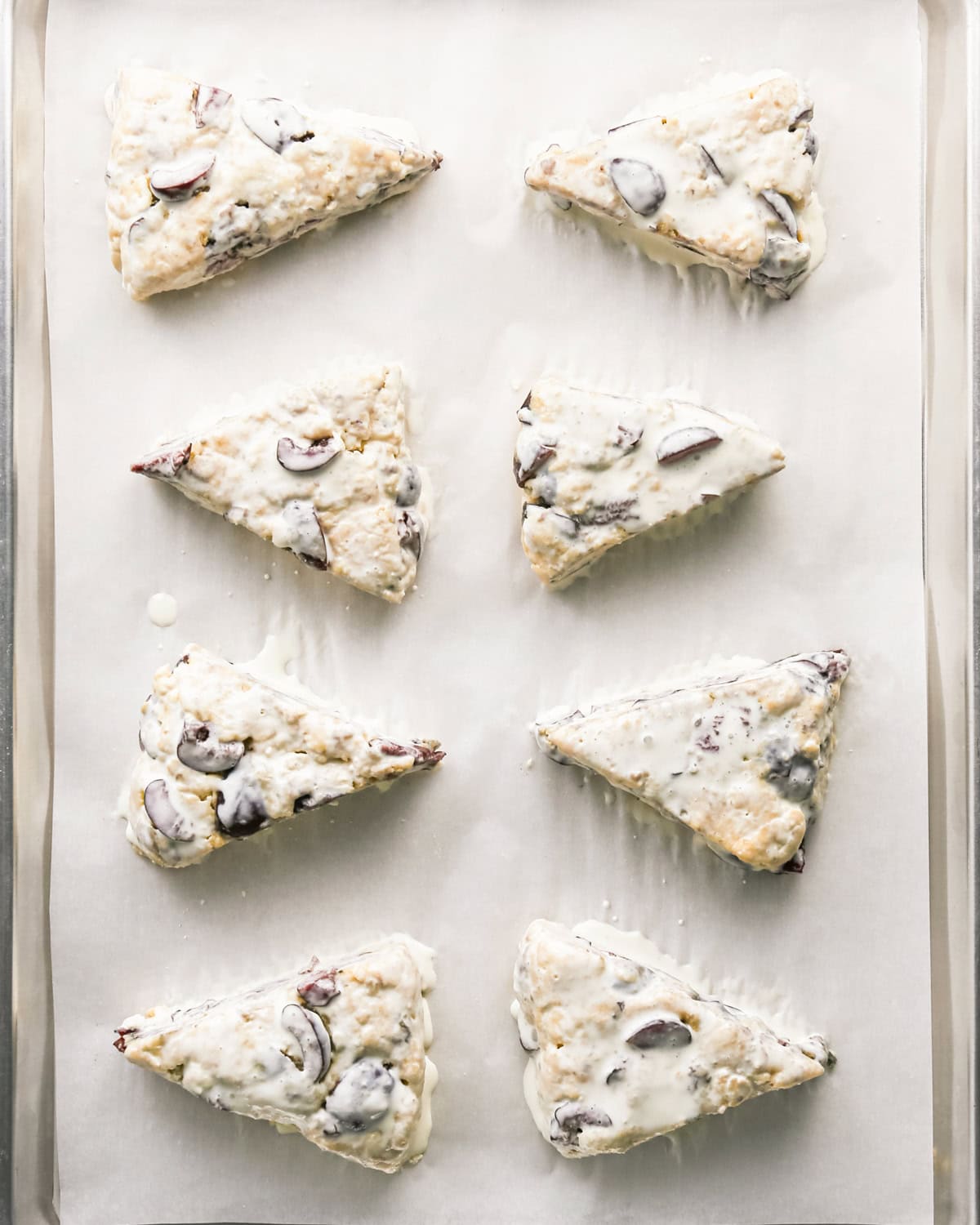 8 unbaked cherry scones brushed with heavy cream on a baking sheet lined with parchment paper