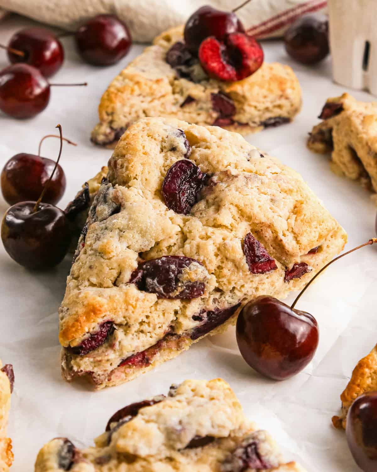 a cherry scone on a piece of parchment paper surrounded by other scones and cherries