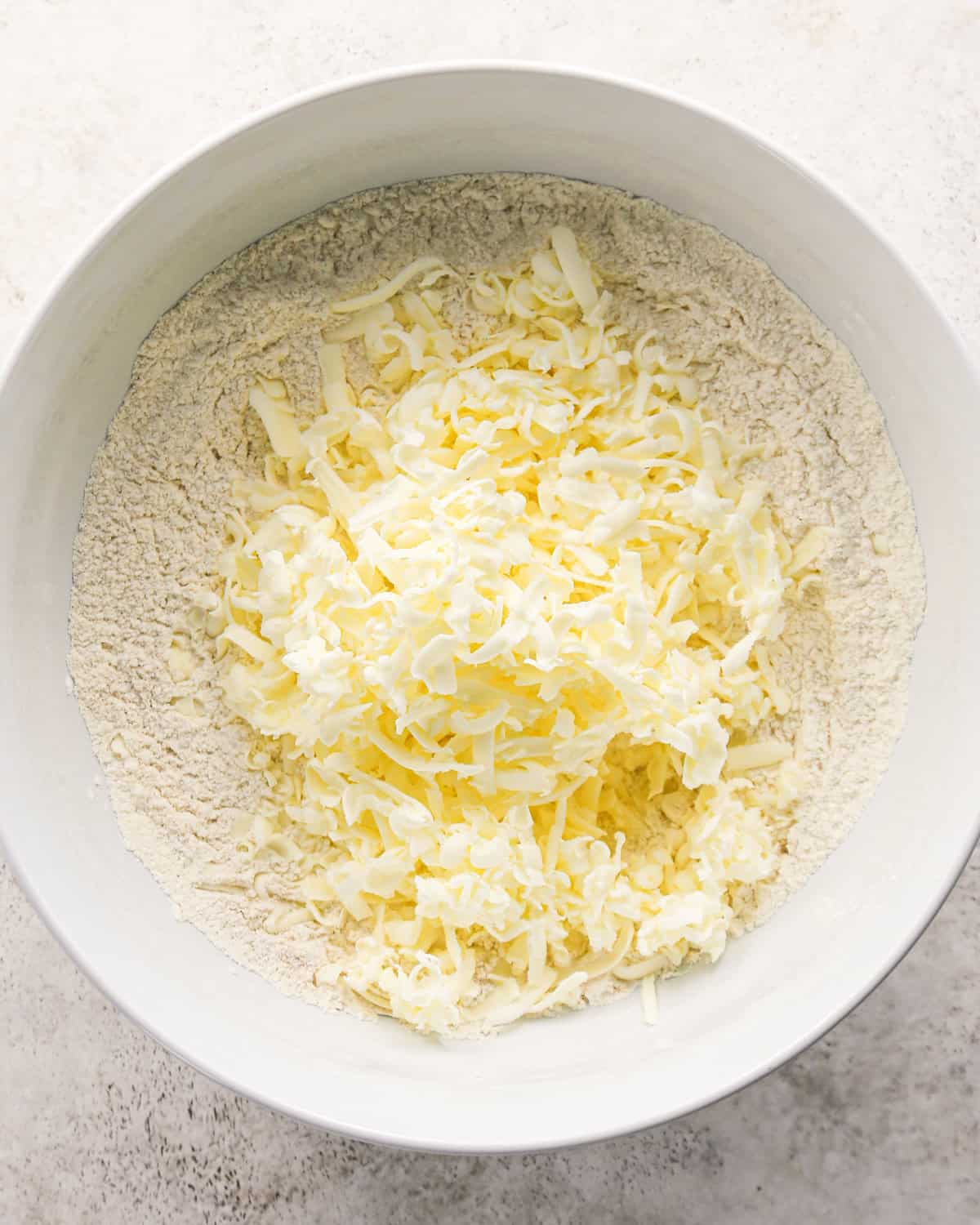 how to make cherry scones - grated frozen butter added to the dry ingredients in a white bowl