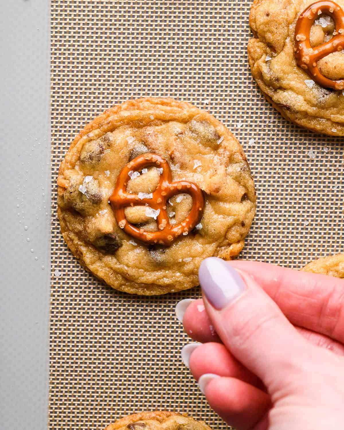 a hand sprinkling flaky sea salt on a Pretzel Cookie