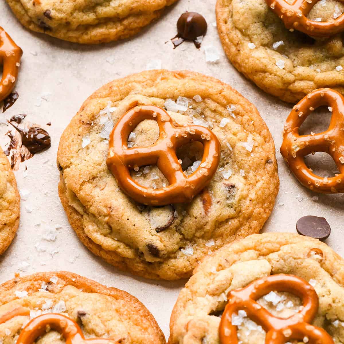 6 chocolate chip pretzel cookies topped with a mini pretzel and a sprinkle of flaky sea salt. surrounded by chocolate chips and pretzels