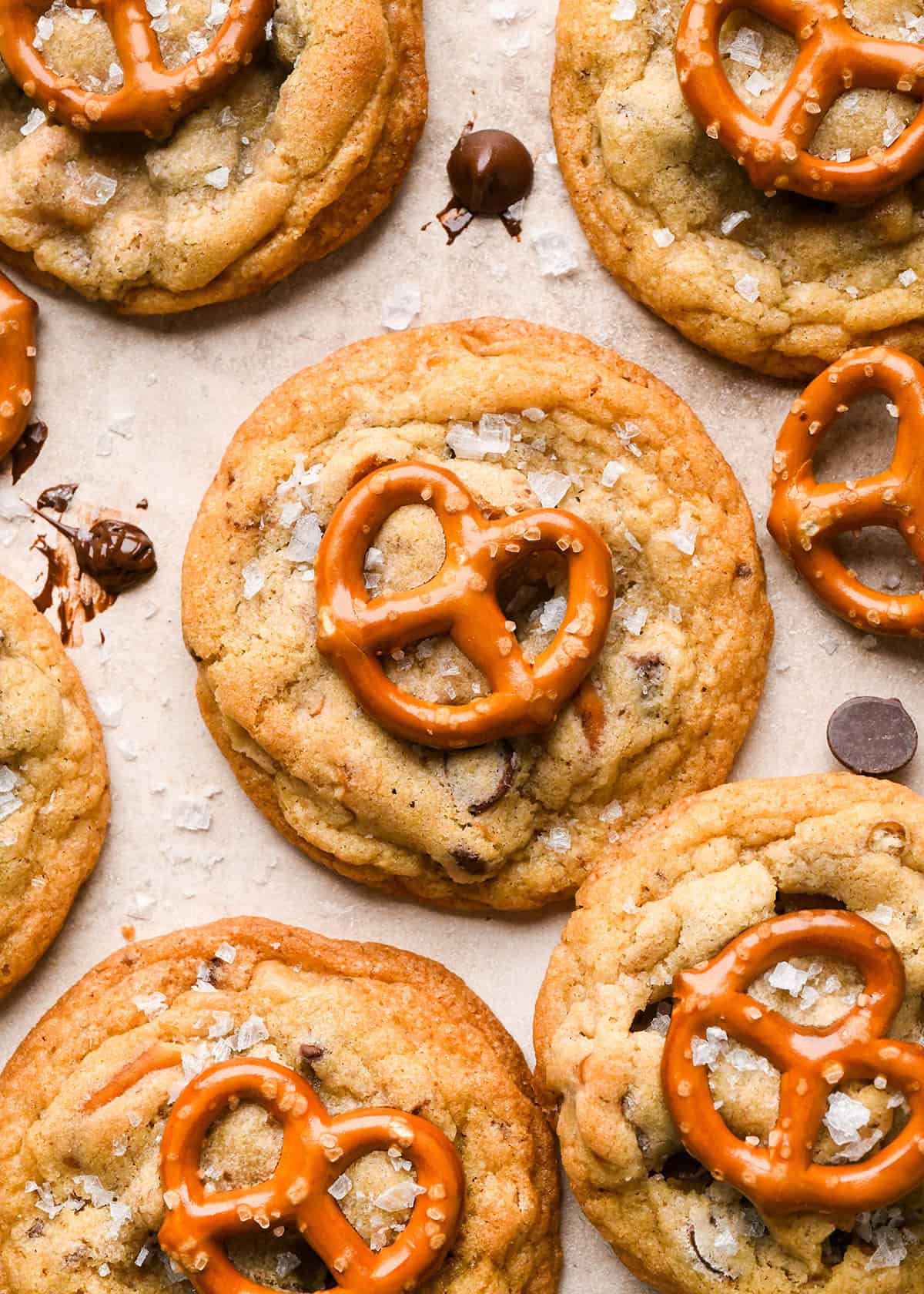 6 chocolate chip pretzel cookies topped with a mini pretzel and a sprinkle of flaky sea salt. surrounded by chocolate chips and pretzels