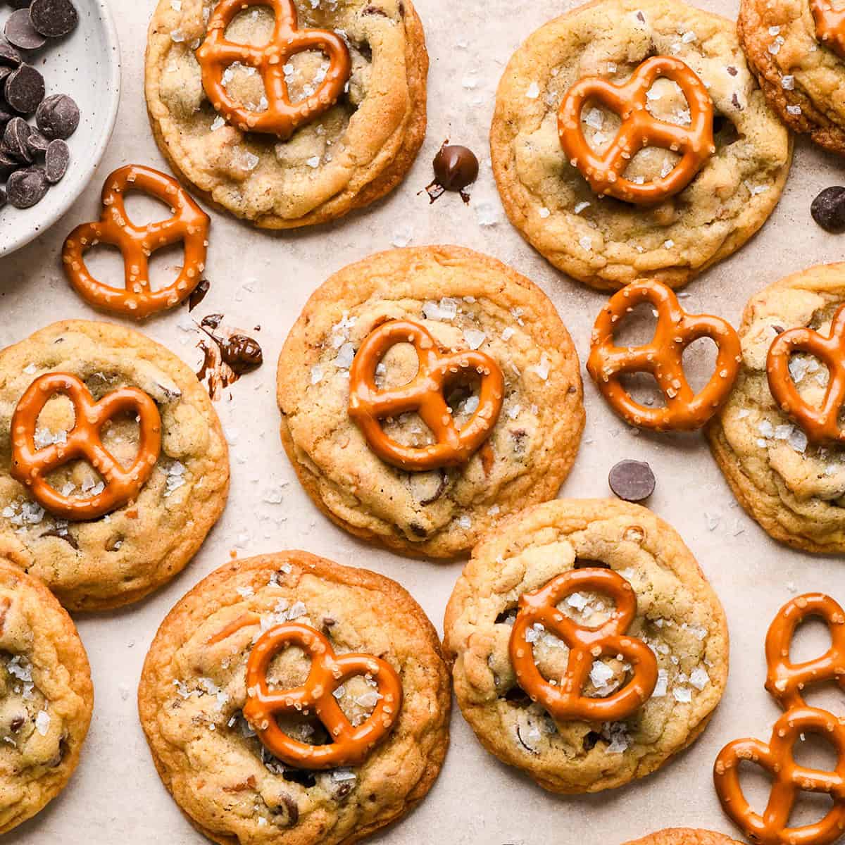 9 chocolate chip pretzel cookies each topped with a mini pretzel and a sprinkle of flaky sea salt. surrounded by chocolate chips and pretzels