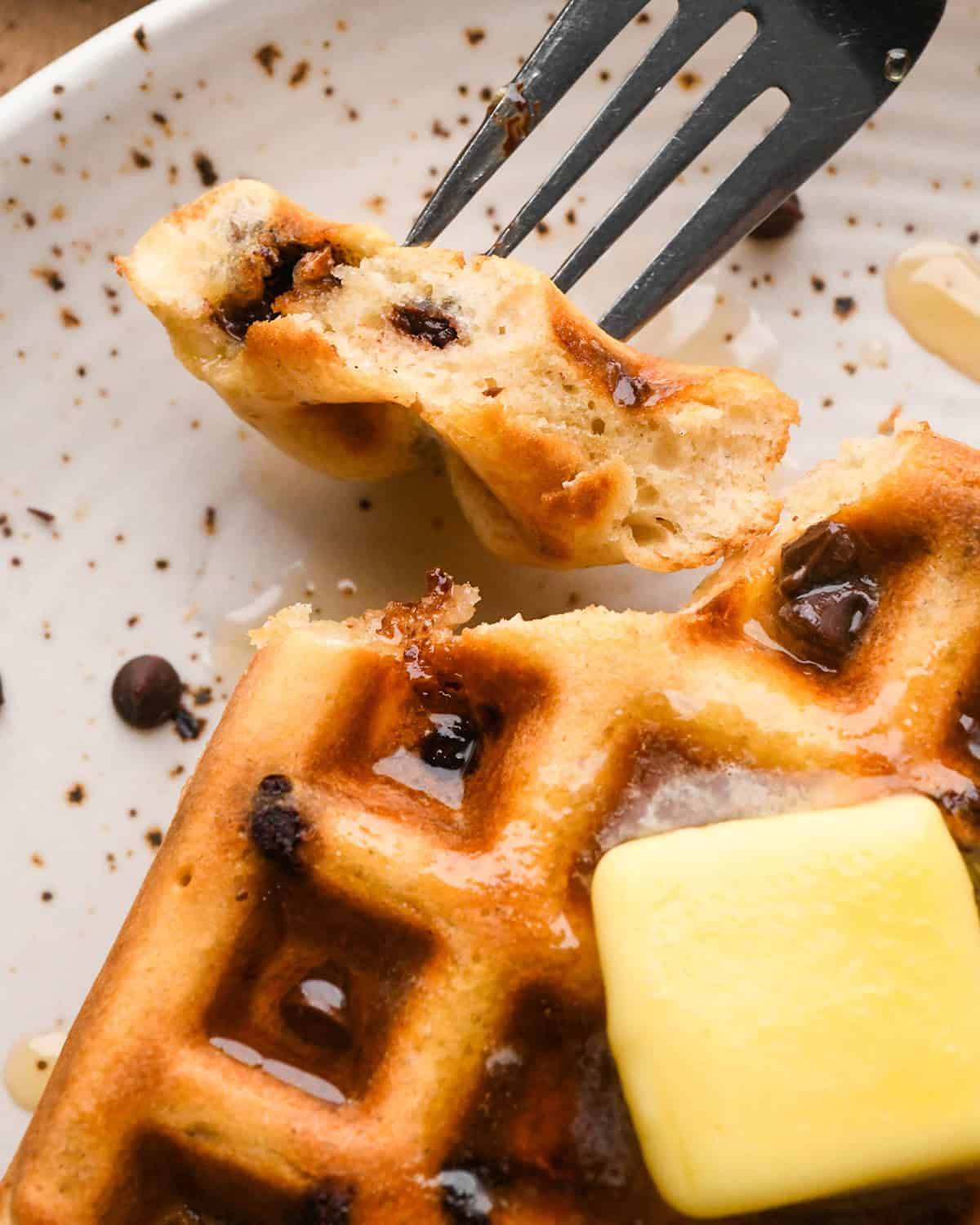 close-up photo of a bite of a chocolate chip waffle on a fork next to a chocolate chip waffle with butter