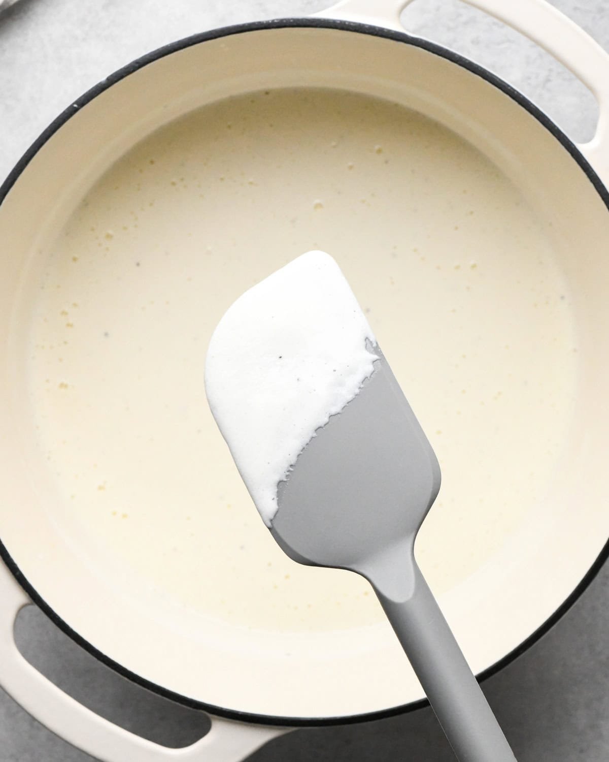 cottage cheese mac and cheese sauce coating a gray spatula being held above the rest of the sauce in a white saucepan