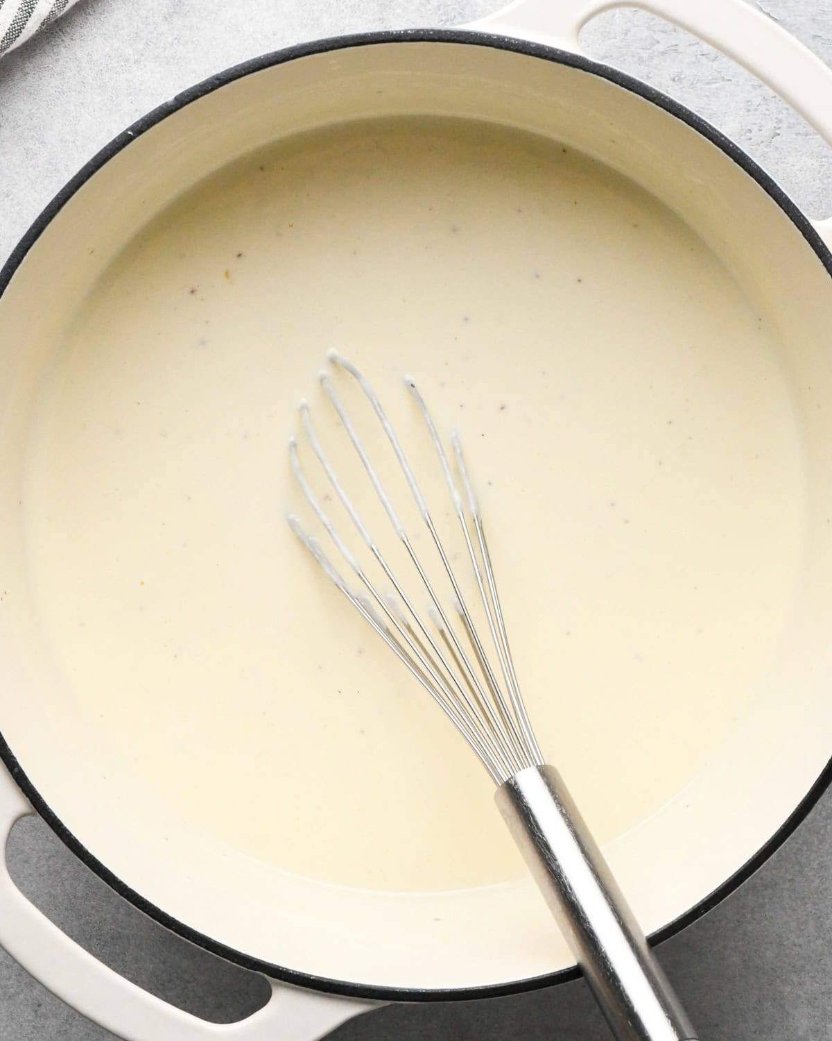 cottage cheese macaroni and cheese sauce with a whisk in a white saucepan