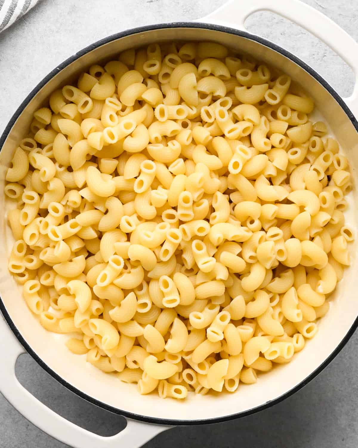 cooked macaroni noodles added to the sauce in a white saucepan making cottage cheese mac and cheese before mixing