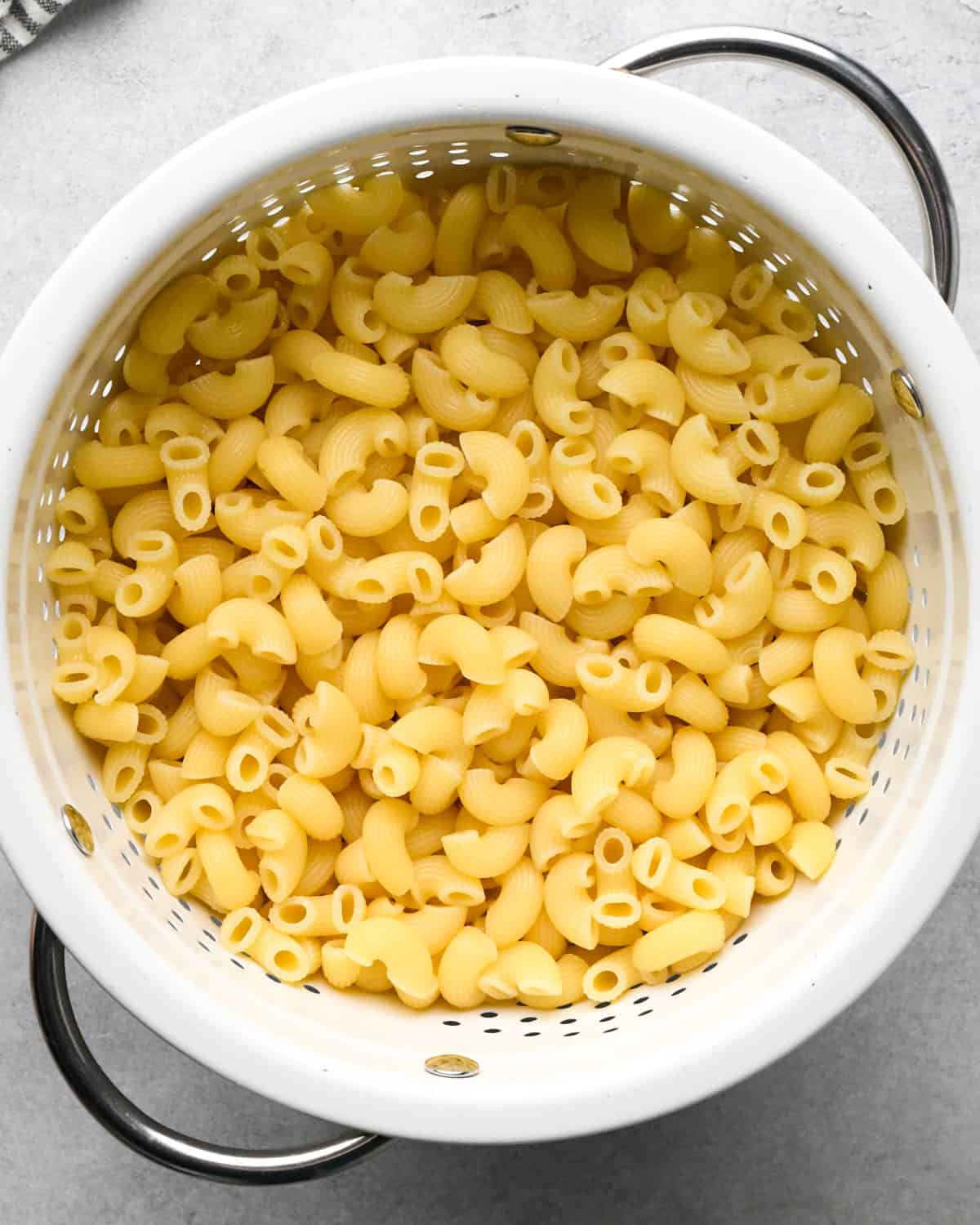cooked elbow macaroni in a white colander with silver handles making cottage cheese mac and cheese