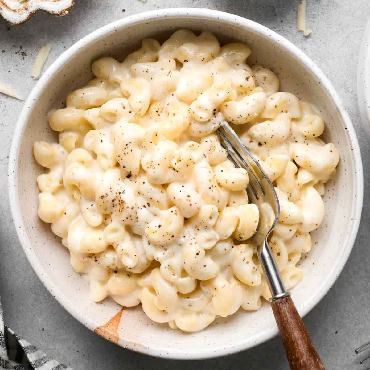 cottage cheese mac and cheese in a ceramic bowl with a fork garnished with freshly ground black pepper