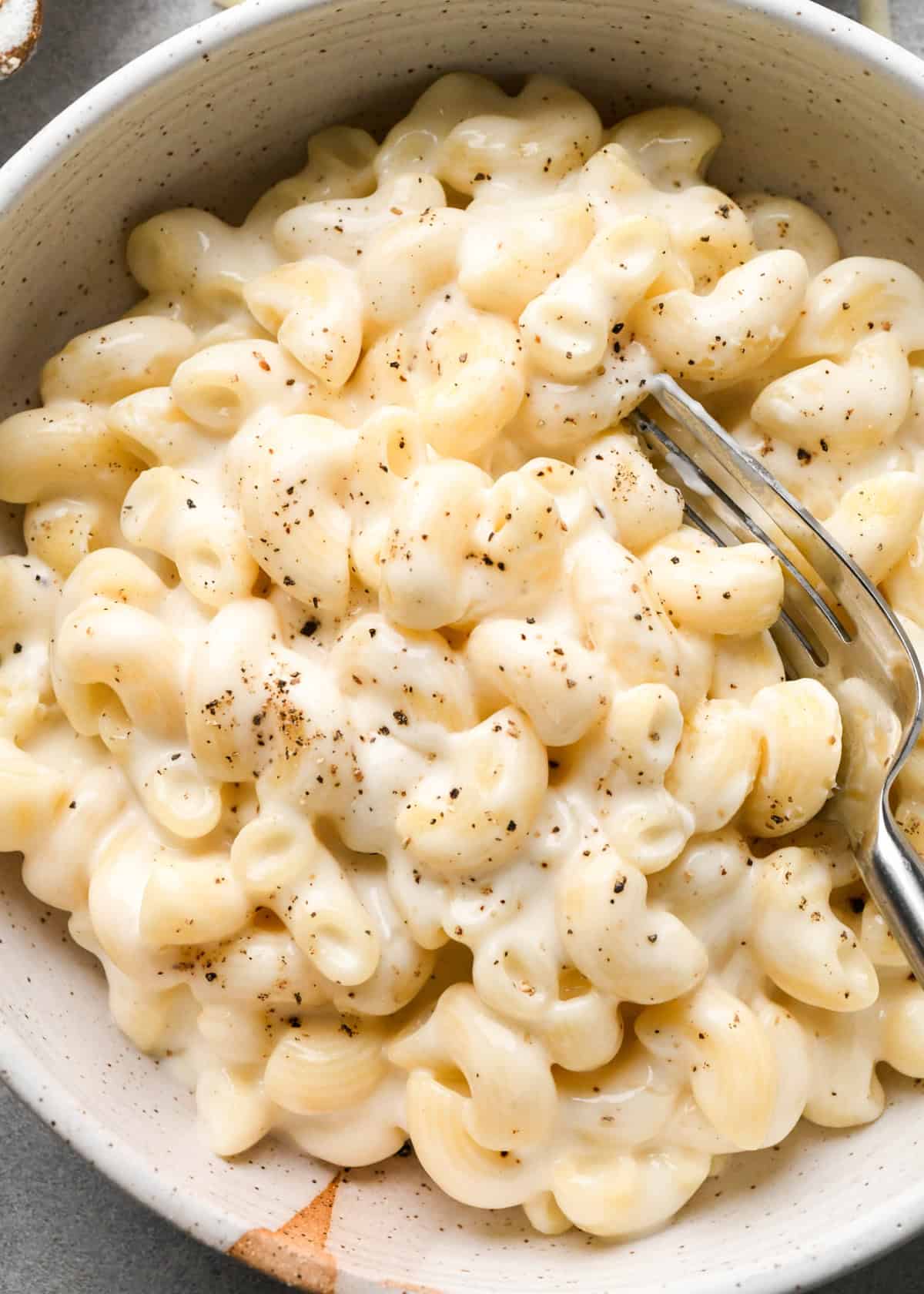 cottage cheese mac and cheese in a ceramic bowl with a fork garnished with freshly ground black pepper