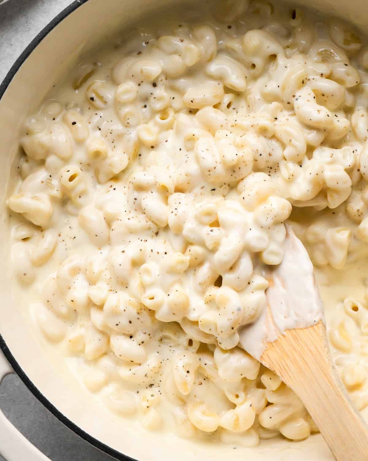 cottage cheese mac and cheese in a white saucepan with a wooden spatula garnished with black pepper