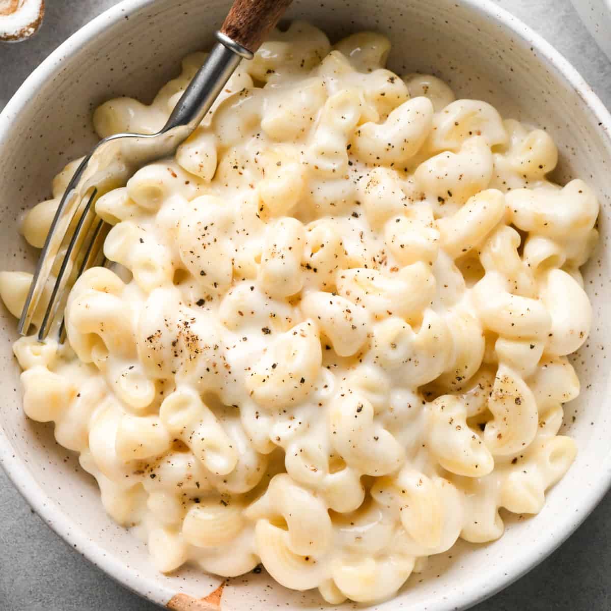 cottage cheese mac and cheese in a ceramic bowl with a fork garnished with freshly ground black pepper