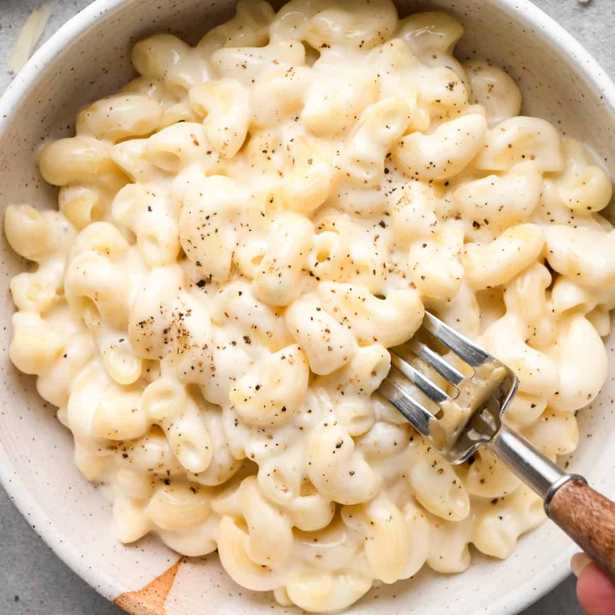 a fork taking a bite of cottage cheese mac and cheese in a ceramic bowl garnished with freshly ground black pepper