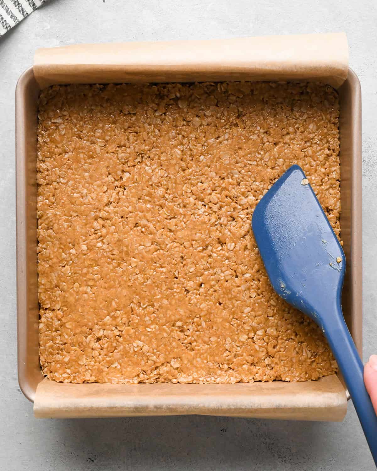making Peanut Butter Granola Bars - bars pressed into the pan with a blue spatula