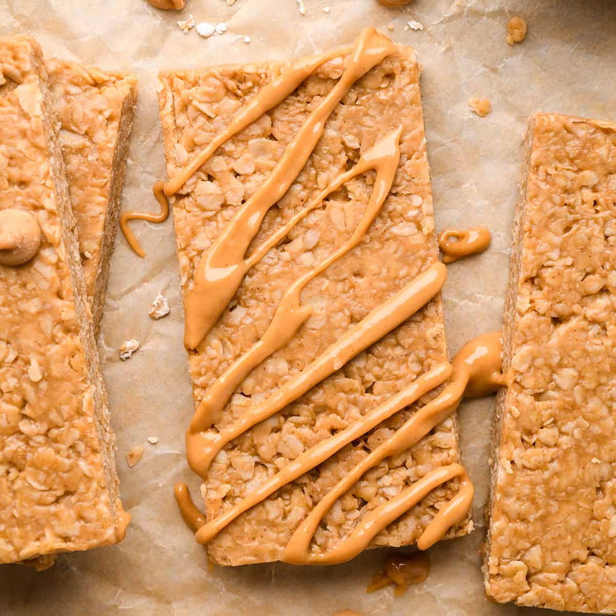 4 Peanut Butter Granola Bars on parchment paper, one with peanut butter drizzle on top 