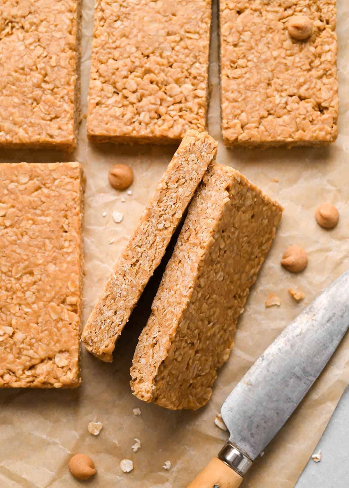 6 Peanut Butter Granola Bars, two turned to the side so the texture is visible on parchment paper with peanut butter chips 