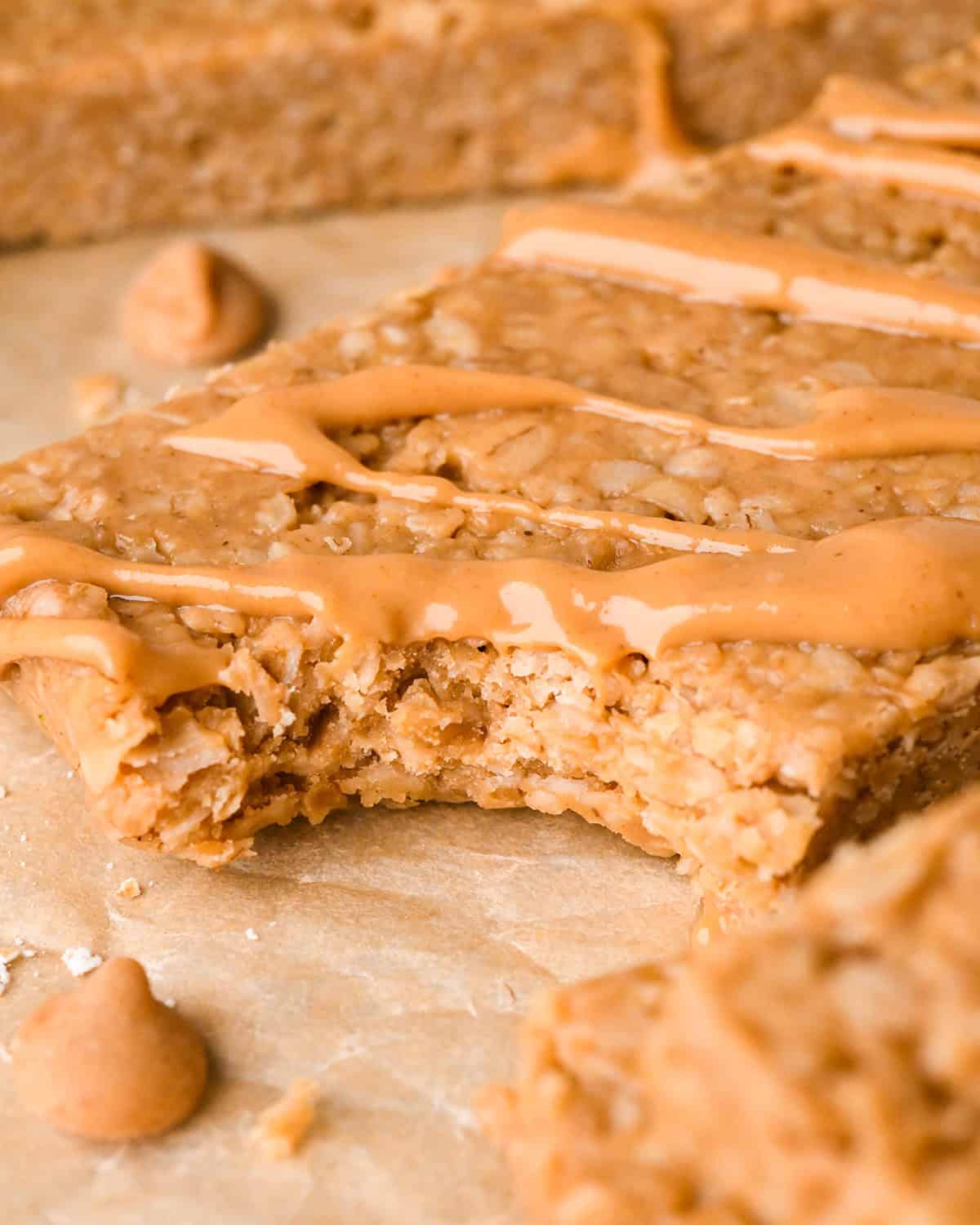 close up of a Peanut Butter Granola Bar with a bite taken out of it and a peanut butter drizzle on top on parchment paper