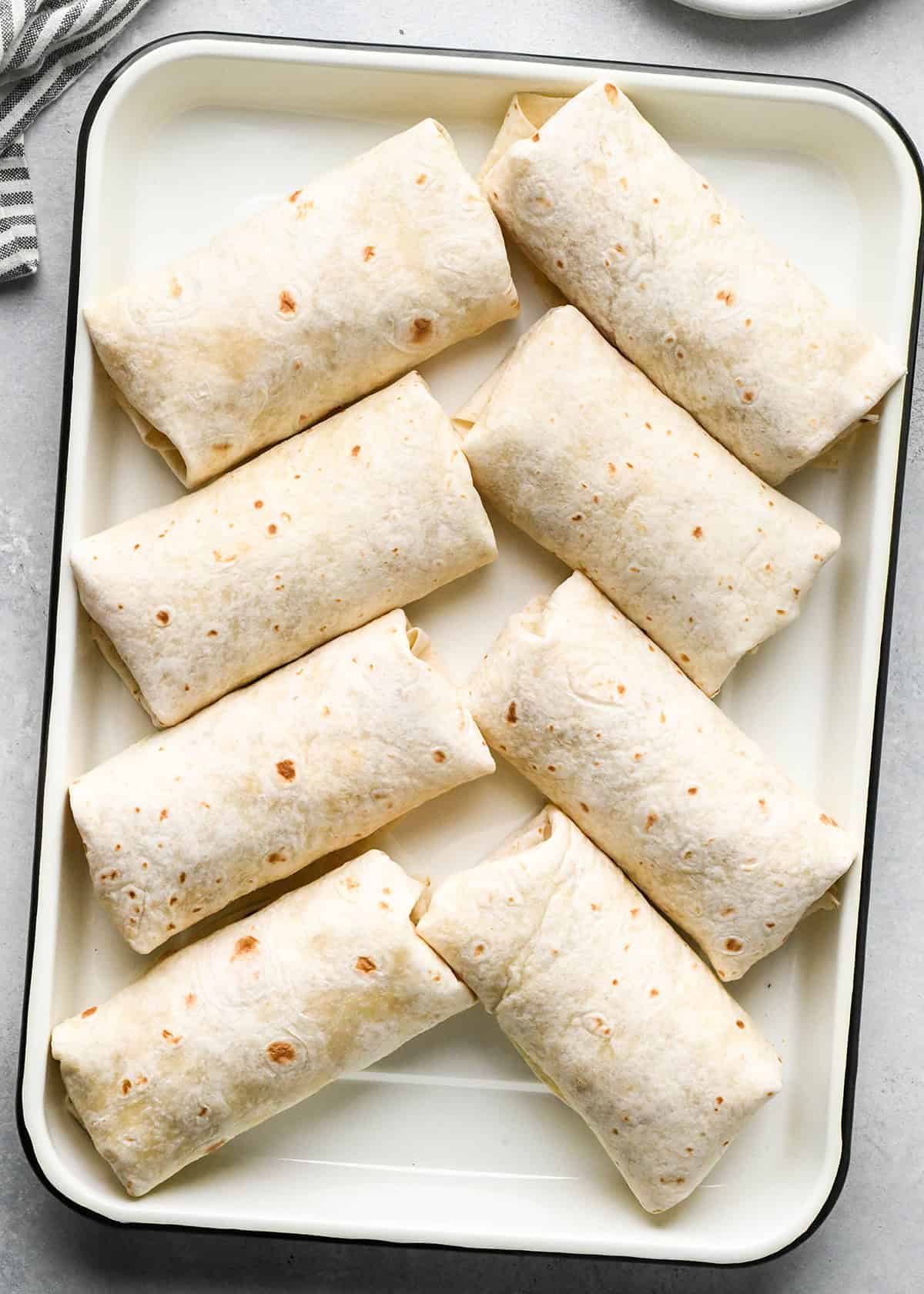 8 breakfast burritos on a baking sheet before baking