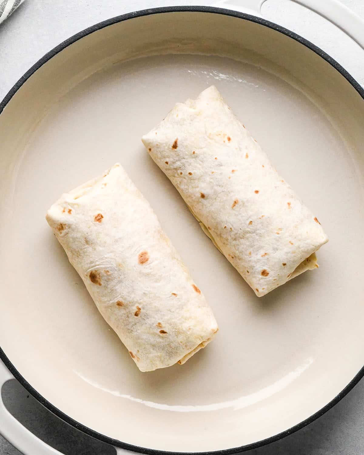 two breakfast burritos cooking on the first side in a skillet