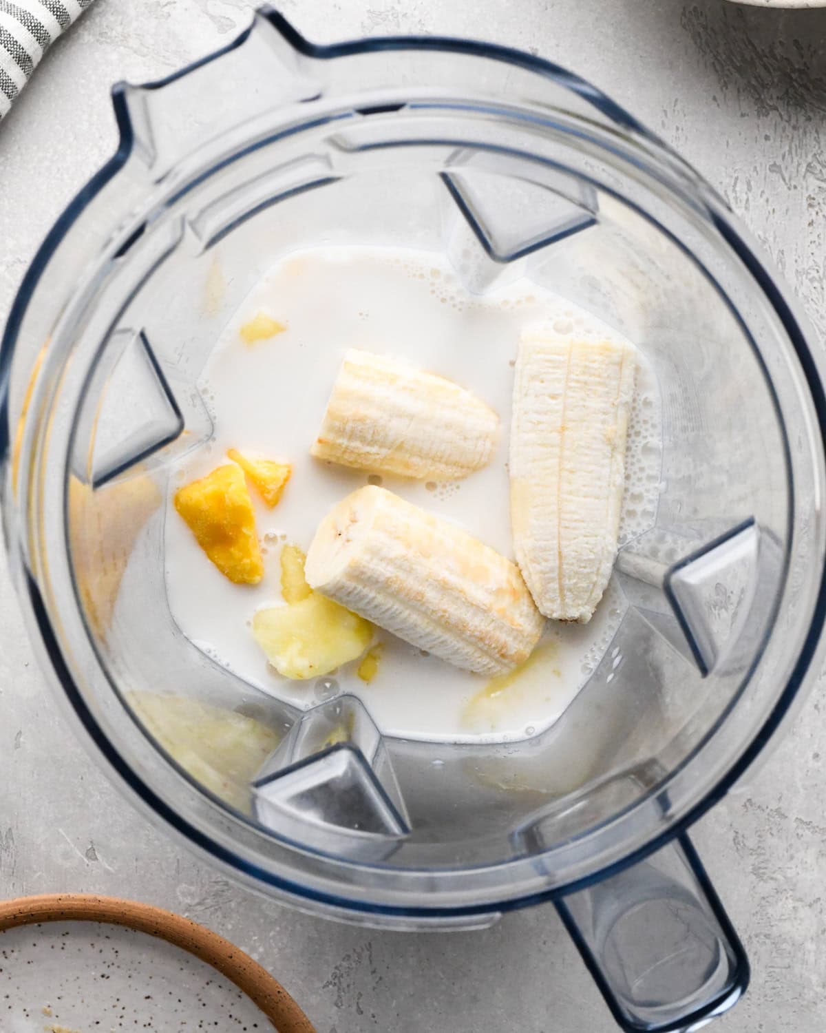 Making kale fruit smoothie: overhead photo of almond milk, bananas, and frozen fruit added to a blender.