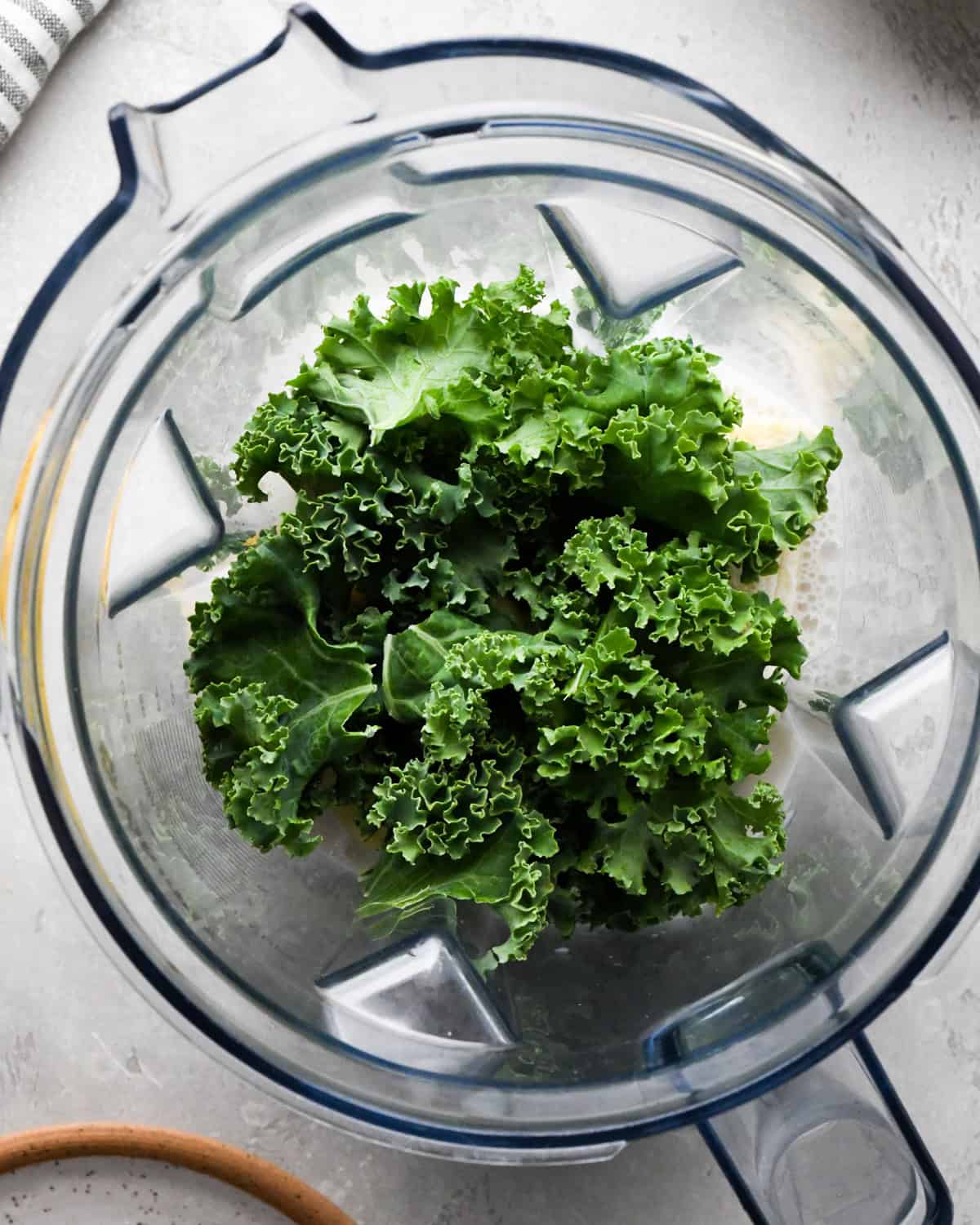 Making kale fruit smoothie: overhead photo of almond milk, bananas, kale, and frozen fruit added to a blender.