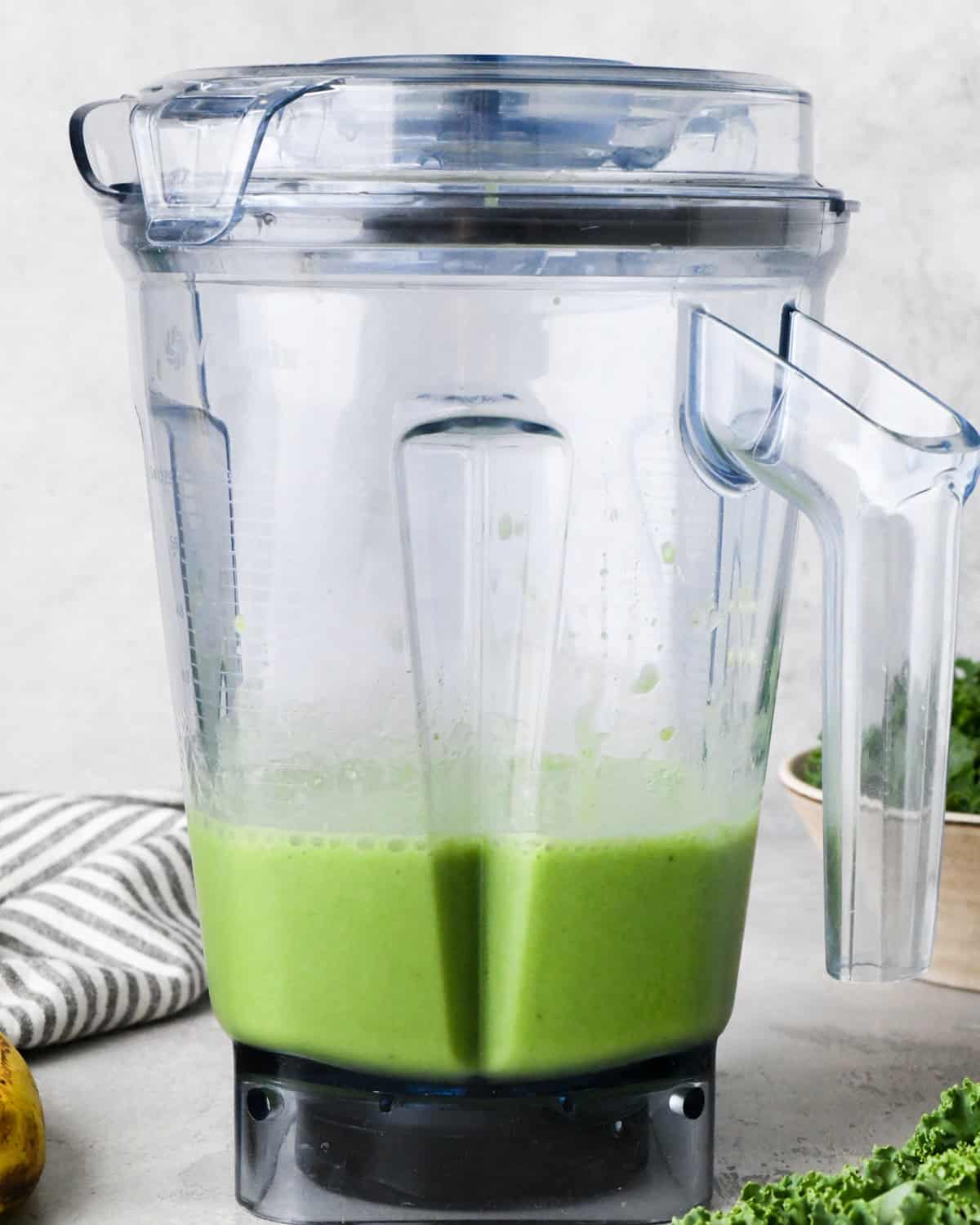 Making kale fruit smoothie: front-view photo of almond milk, bananas, kale, and frozen fruit added to a blender and blended together.