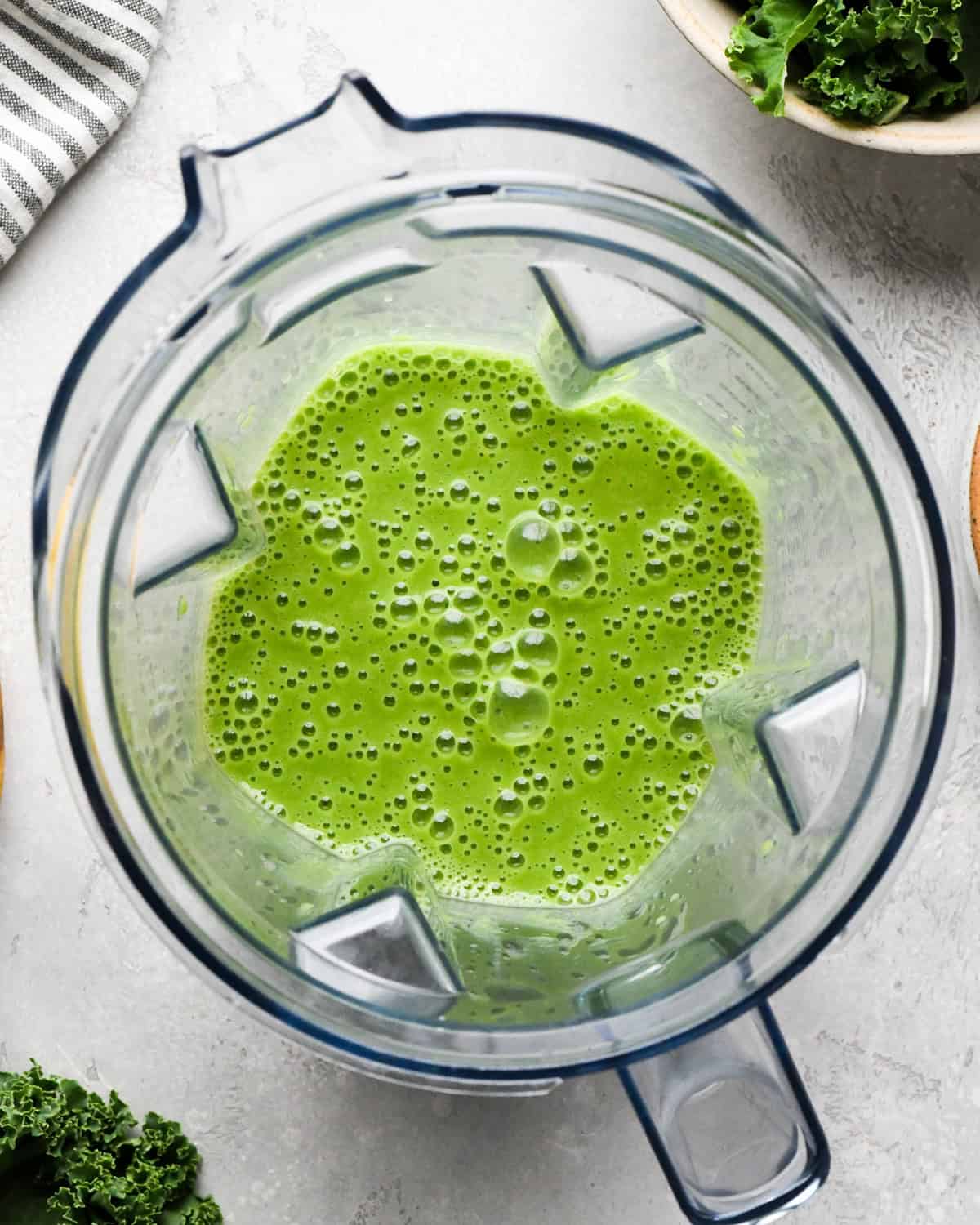 Making kale fruit smoothie: overhead photo of almond milk, bananas, kale, and frozen fruit added to a blender and blended together.