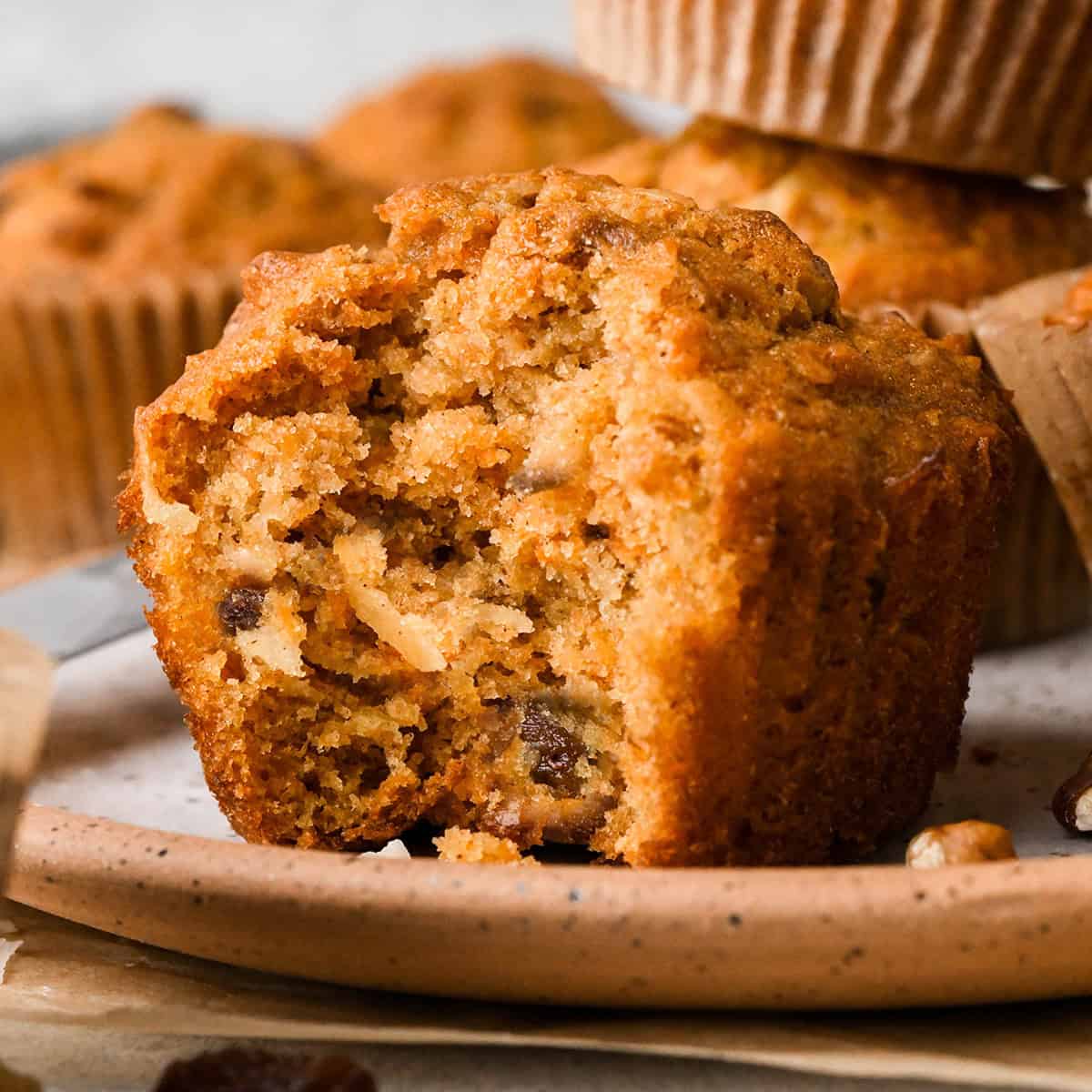 a Morning Glory Muffin with a bite taken out of it showing the inside texture with grated carrots, apples, raisins, coconut, and chopped nuts