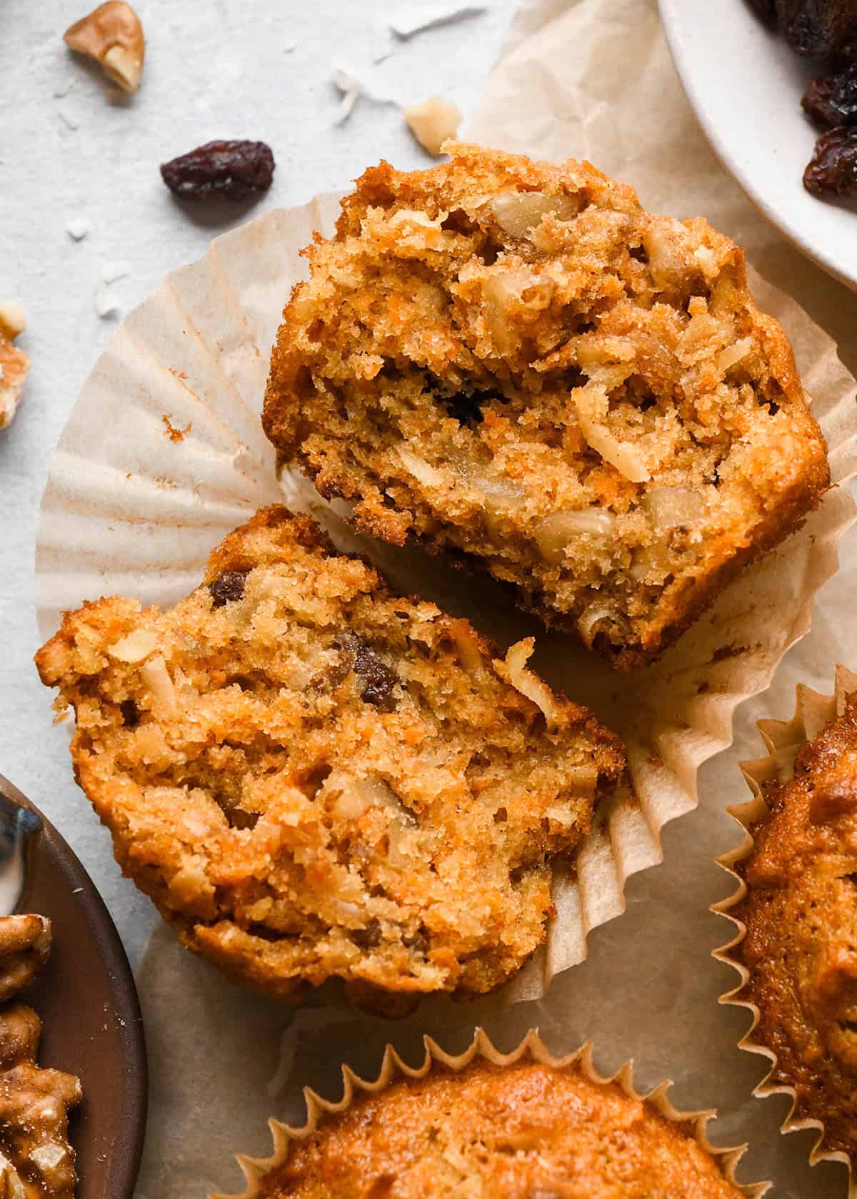 Close-up of a morning glory muffin cut in half on a muffin wrapper, showing the texture filled with grated carrots, apples, raisins, coconut, and chopped nuts