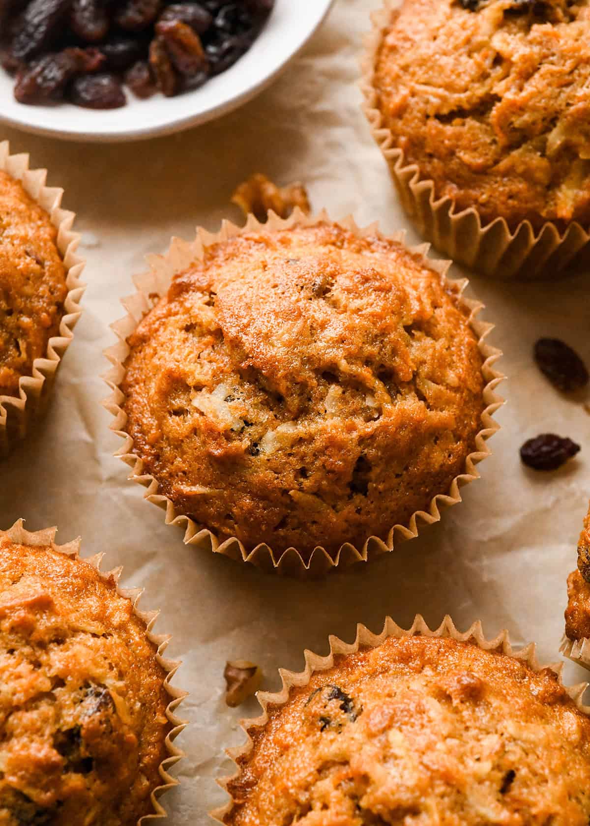 5 morning glory muffins on parchment paper surrounded by raisins and nuts