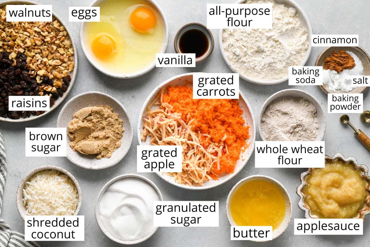 overhead photo of the labeled ingredients in this Morning Glory Muffins recipe like grated carrots, grated apples, coconut, raisins, walnuts, flour, applesauce, eggs, butter and more
