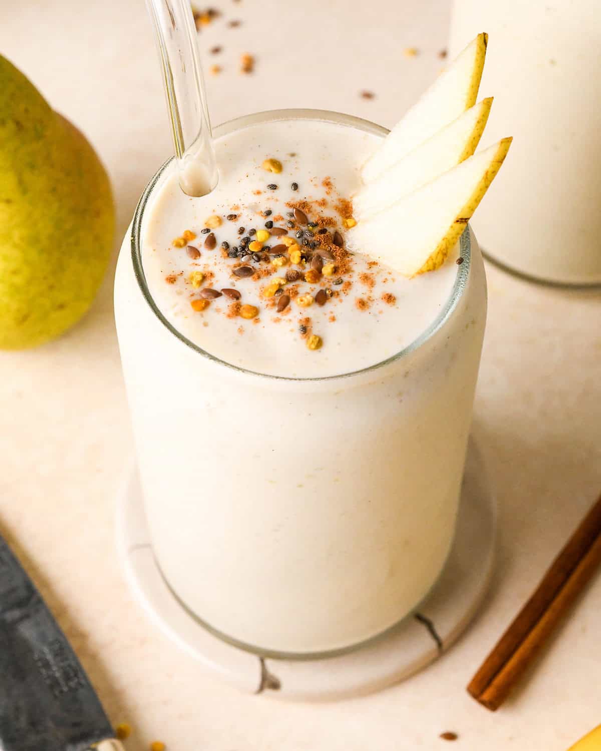 Pear Smoothie in a glass topped with pears, chia seeds, bee pollen and cinnamon surrounded by another glass of smoothie, a pear and cinnamon stick