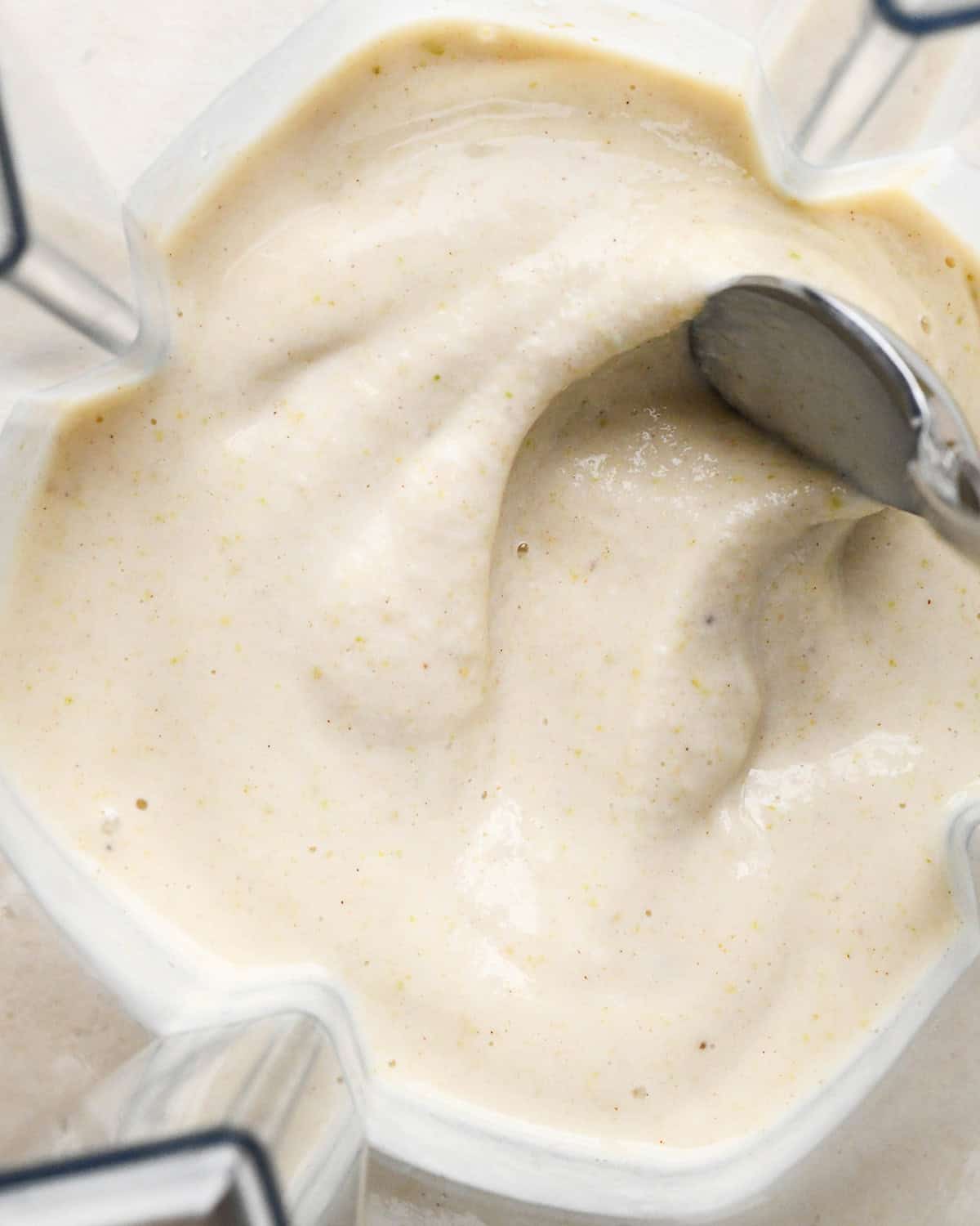 Pear Smoothie in a blending container with a spoon showing its thick texture