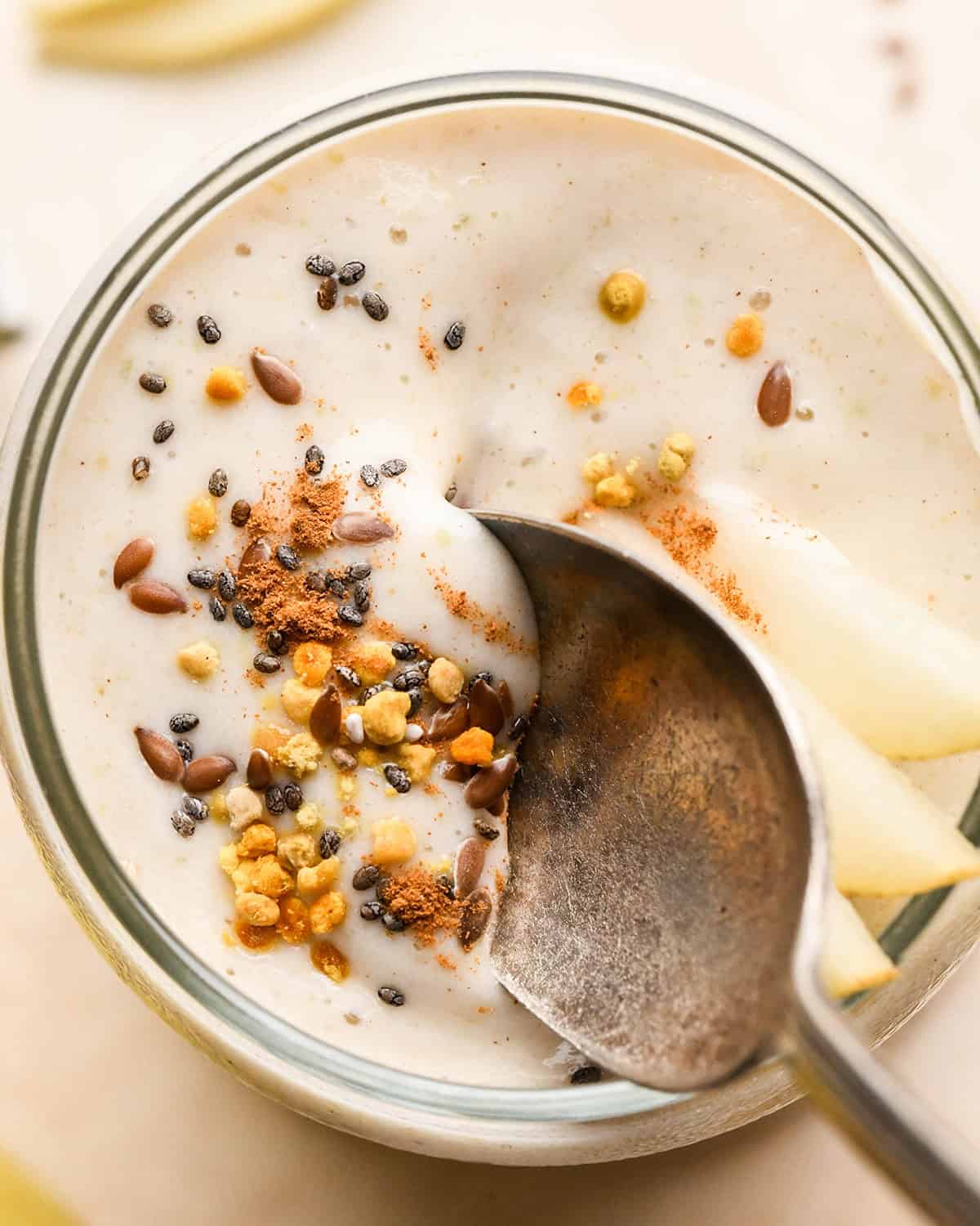 a spoon taking a bite of Pear Smoothie in a glass topped with pears, chia seeds, bee pollen and cinnamon 