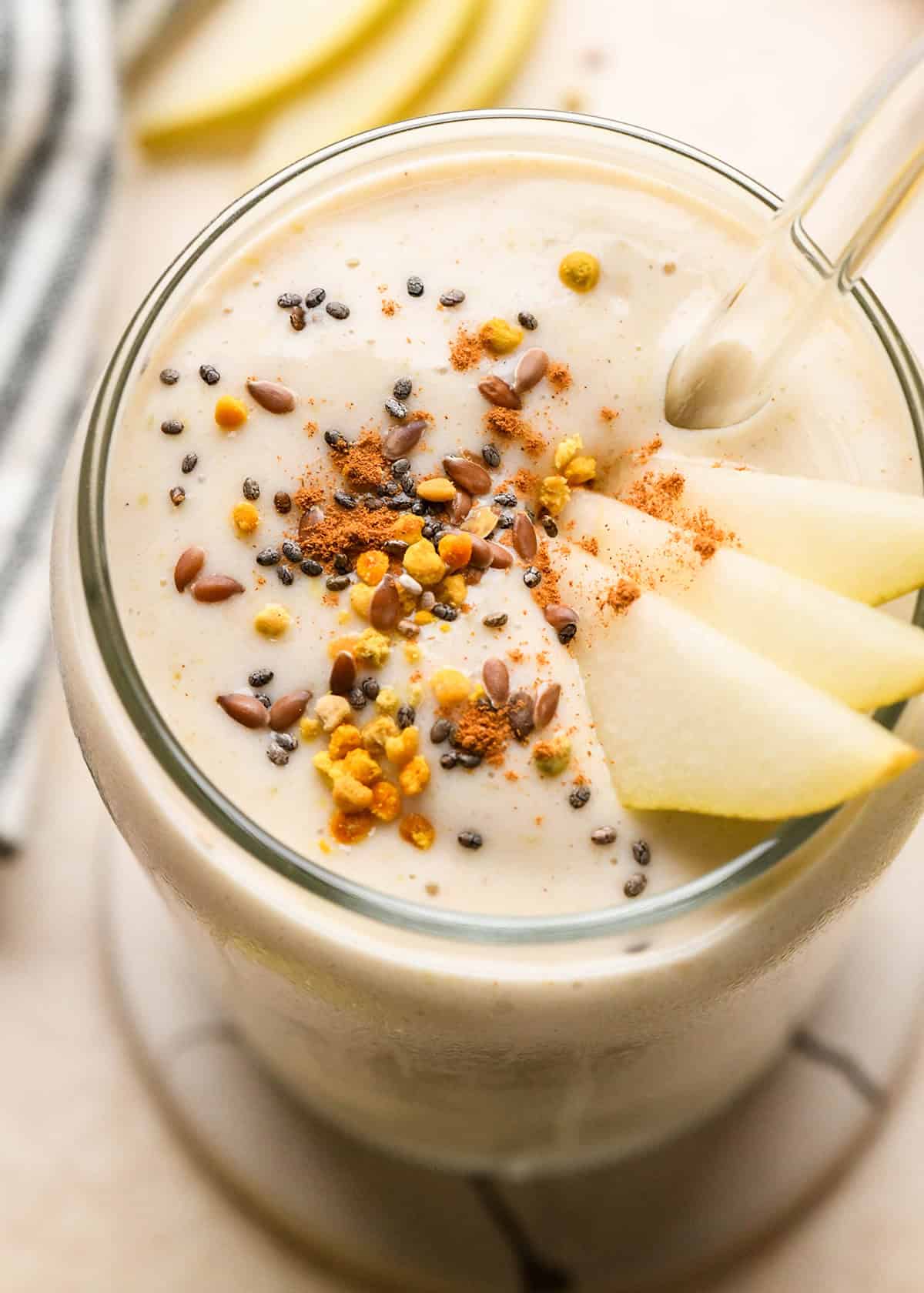 up close photo of Pear Smoothie in a glass topped with pears, chia seeds, bee pollen and cinnamon  with a glass straw
