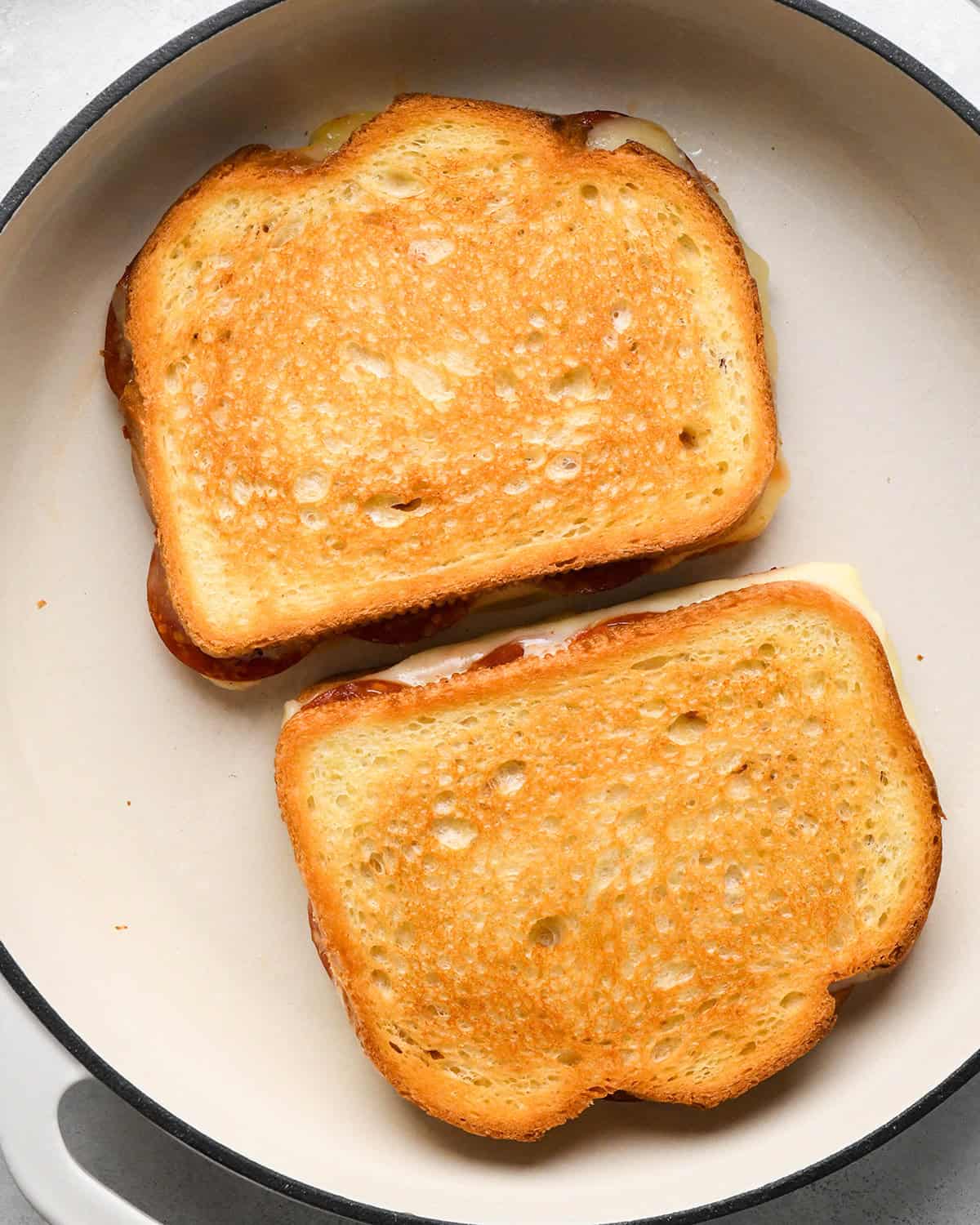 two pizza grilled cheese sandwiches cooking in a pan on the second side 