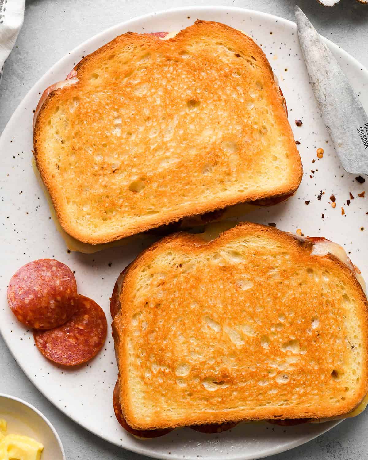 two cooked pizza grilled cheese sandwiches on a white plate with pepperoni and red pepper flakes