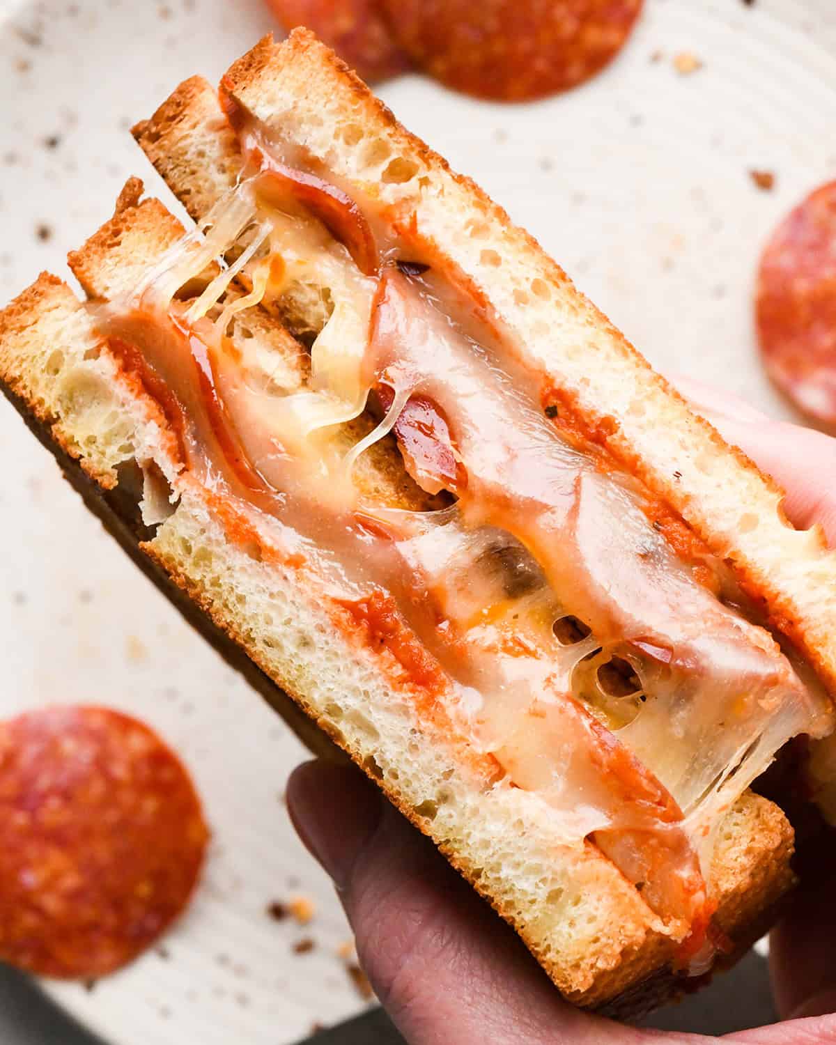 a hand holding two halves of Pizza Grilled Cheese so the melty, cheesy inside is showing styled with pepperoni