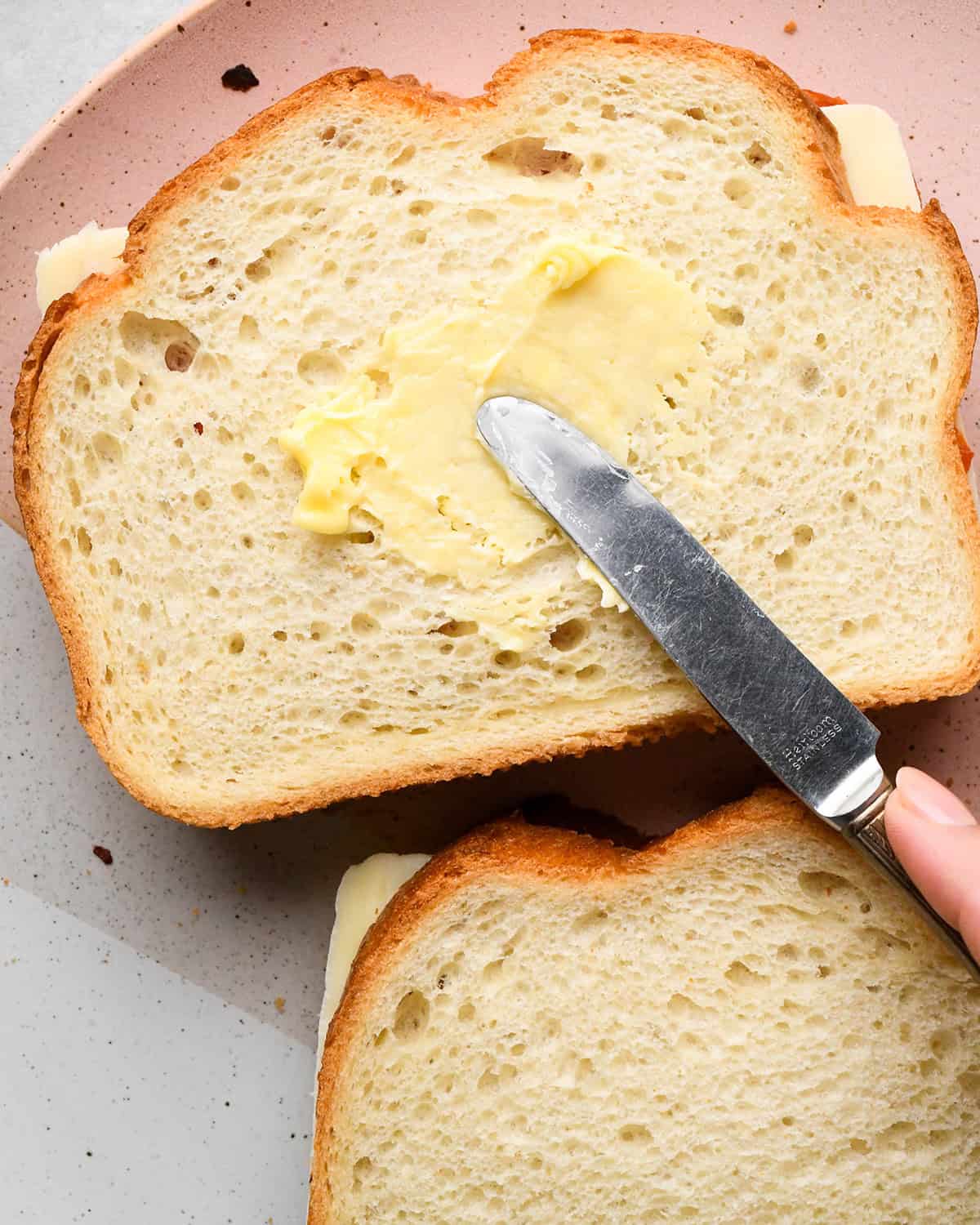 butter being spread on one assembled pizza grilled cheese sandwich 
