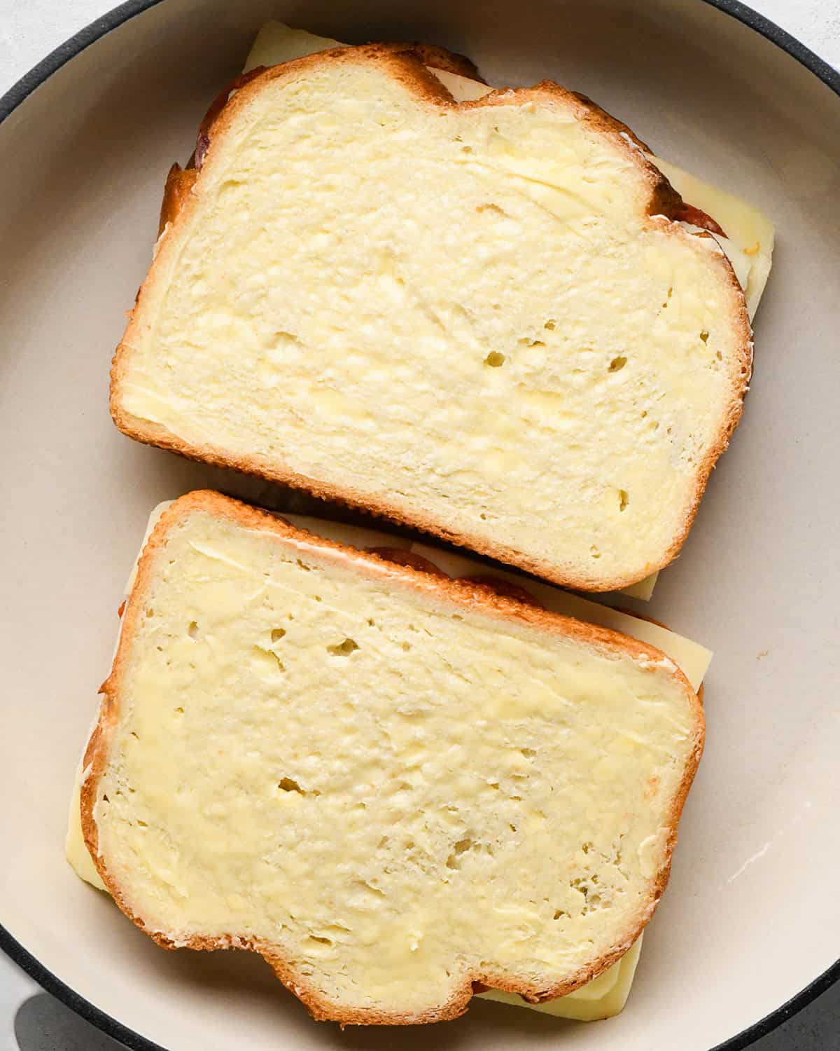 two assembled pizza grilled cheese sandwiches cooking in a pan on the first side 