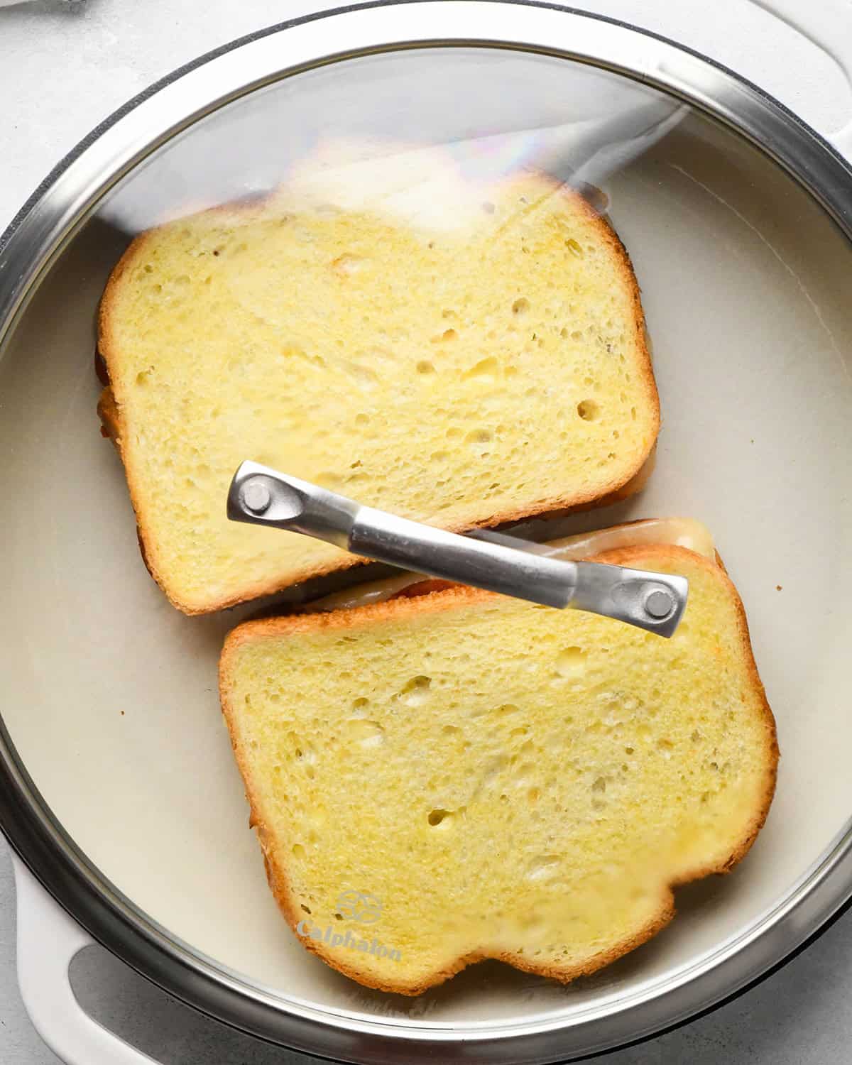 two assembled pizza grilled cheese sandwiches cooking in a pan on the first side covered 
