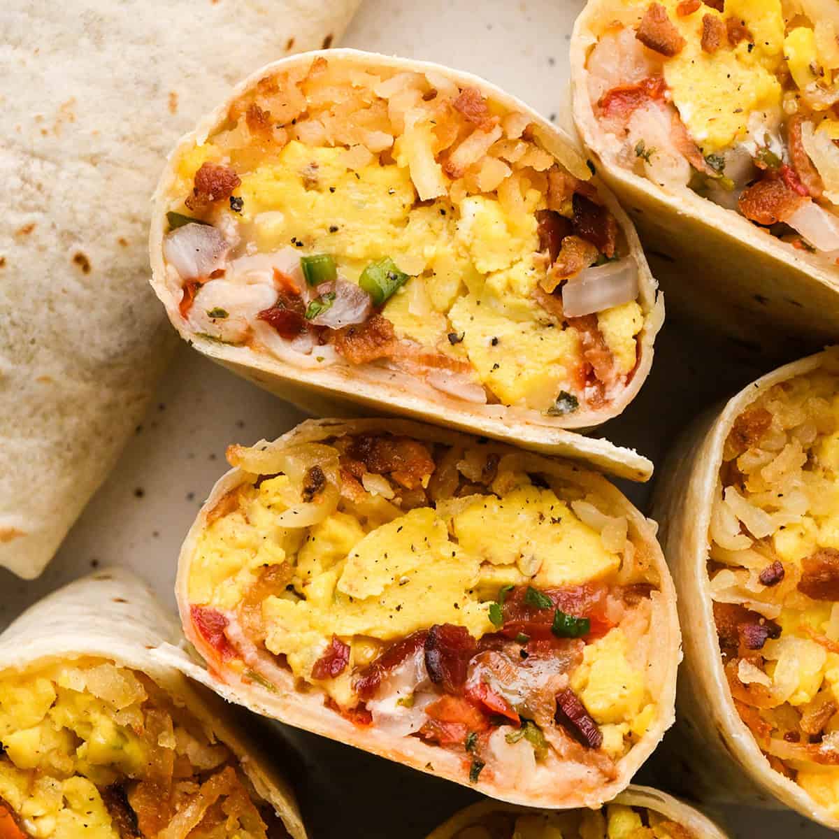 Close-up of 6 breakfast burritos sliced in half filled with scrambled eggs, hash browns, bacon, and cheese