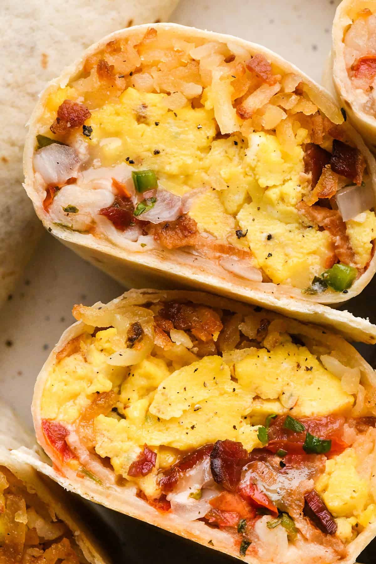 up close photo of Breakfast Burritos cut in half Close-up of filled with scrambled eggs, hash browns, bacon, and cheese