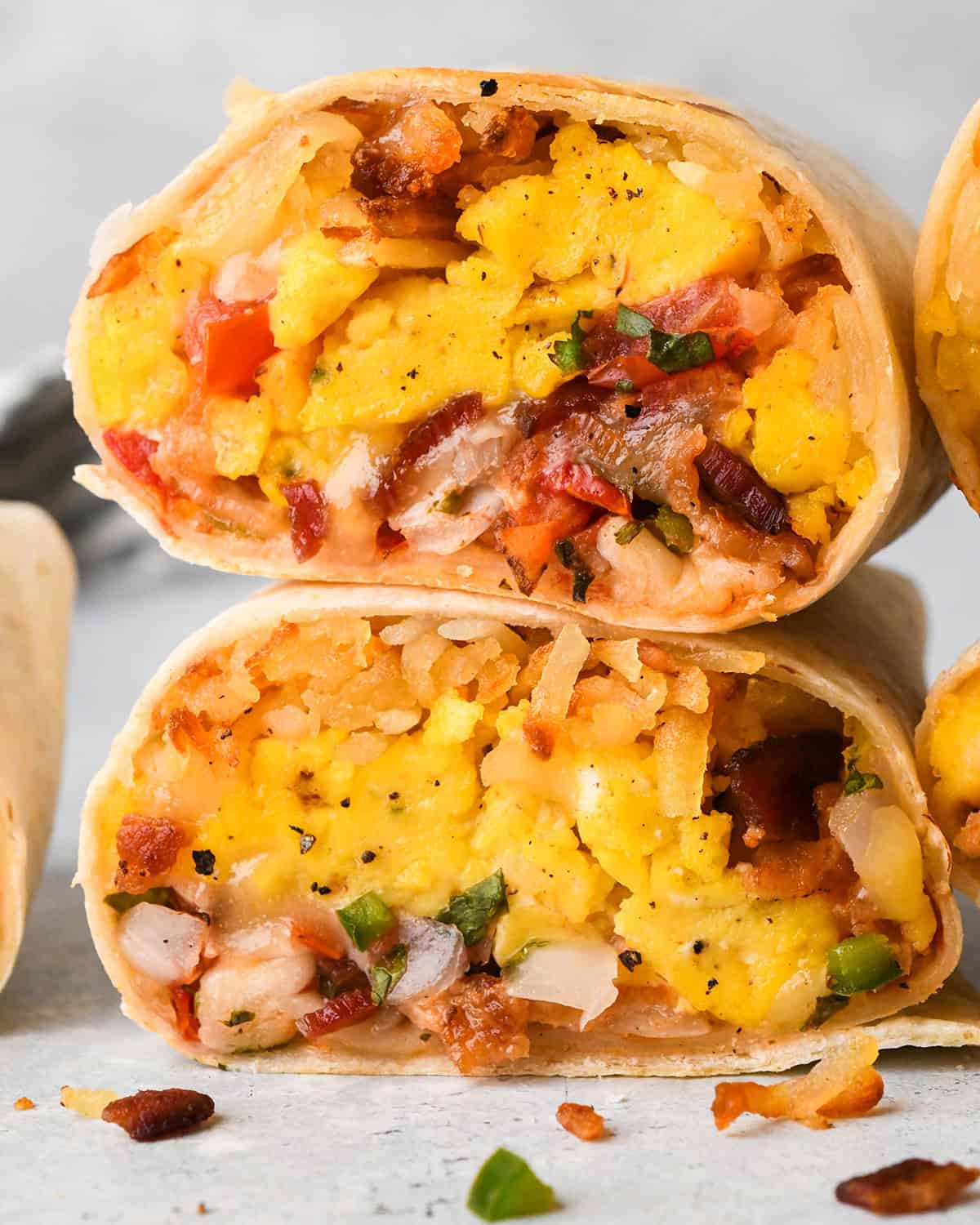 a stack of 2 Breakfast Burritos sliced in half filled with scrambled eggs, hash browns, bacon, and cheese