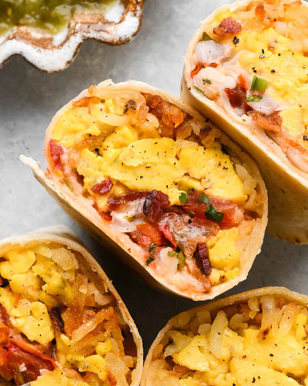 4 Breakfast Burritos sliced in half filled with scrambled eggs, hash browns, bacon, and cheese