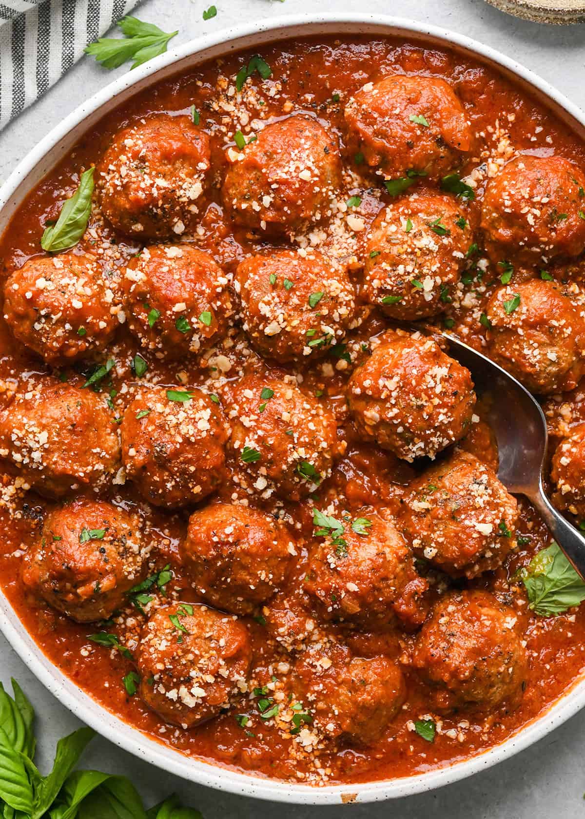 Slow Cooker Meatballs in marinara sauce in a bowl with a spoon, garnished with parmesan cheese and basil