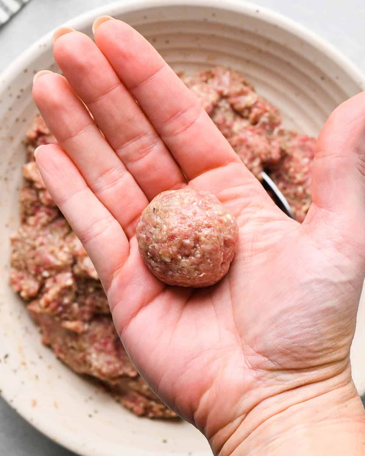 making slow cooker meatballs - a hand holding an uncooked meatball