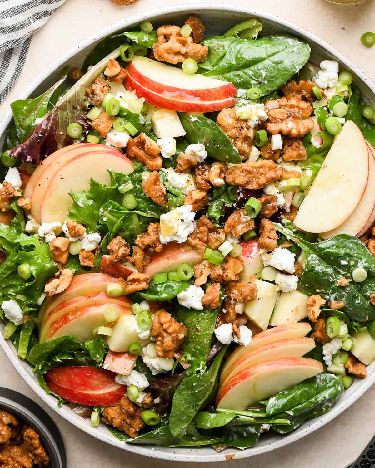 apple salad in a serving bowl topped with sliced apples, goat cheese, walnuts and green onions and vinaigrette dressing