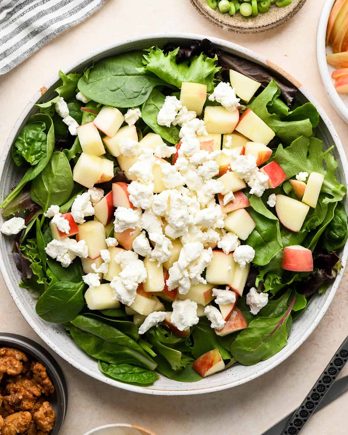 assembling apple salad - goat cheese and apples on top of spring mix in a bowl